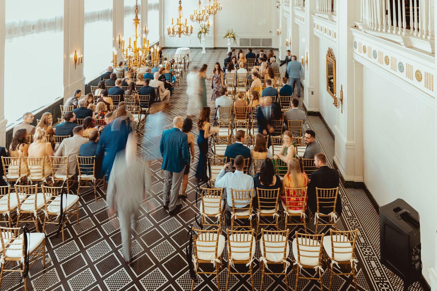 Wedding ceremony venue with gold chandeliers and rows of chairs being set up for guests.
