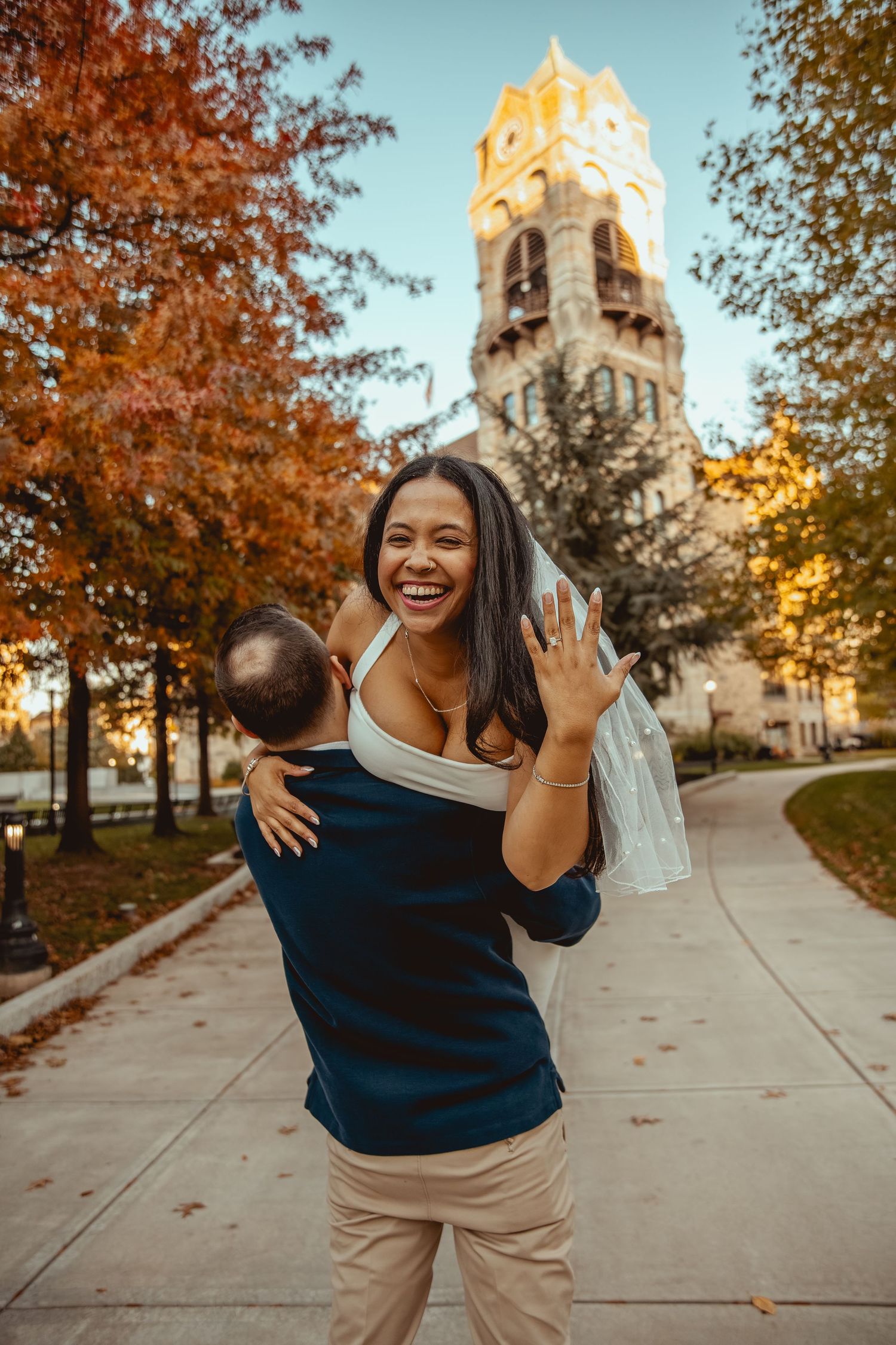 Joyful moments captured on a college campus walkway during autumn with golden fall foliage and a church tower in background.