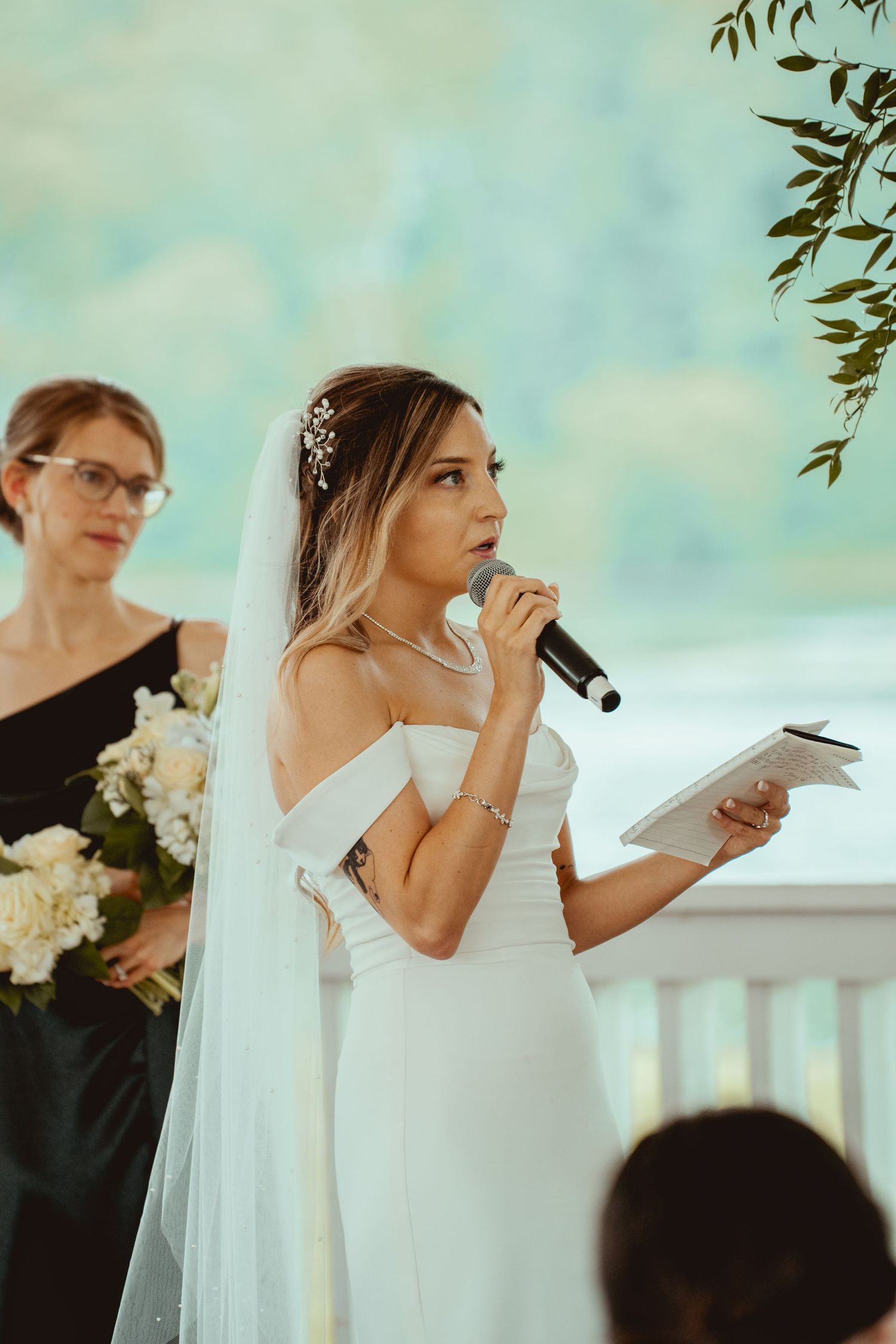 An emotional wedding ceremony moment as a bride wipes away tears while reading vows at an outdoor venue.