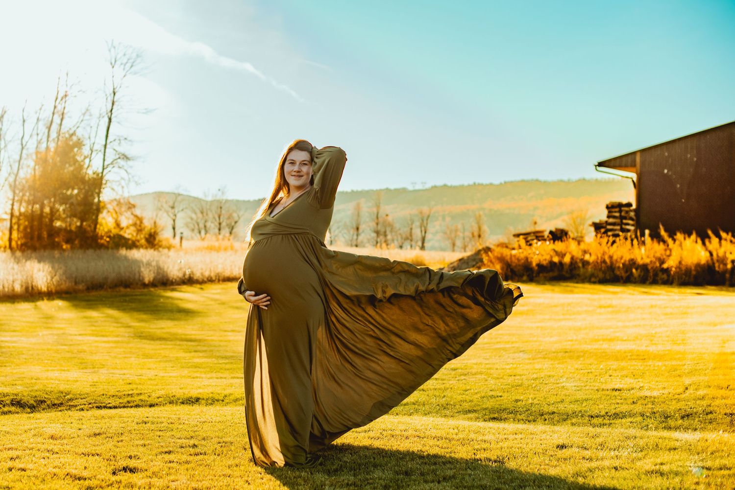 A flowing dress billows in the wind against a golden sunset landscape with mountains in the background.