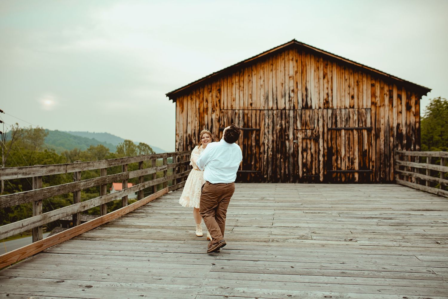 A weathered wooden boardwalk leads to an old barn structure under an overcast sky.