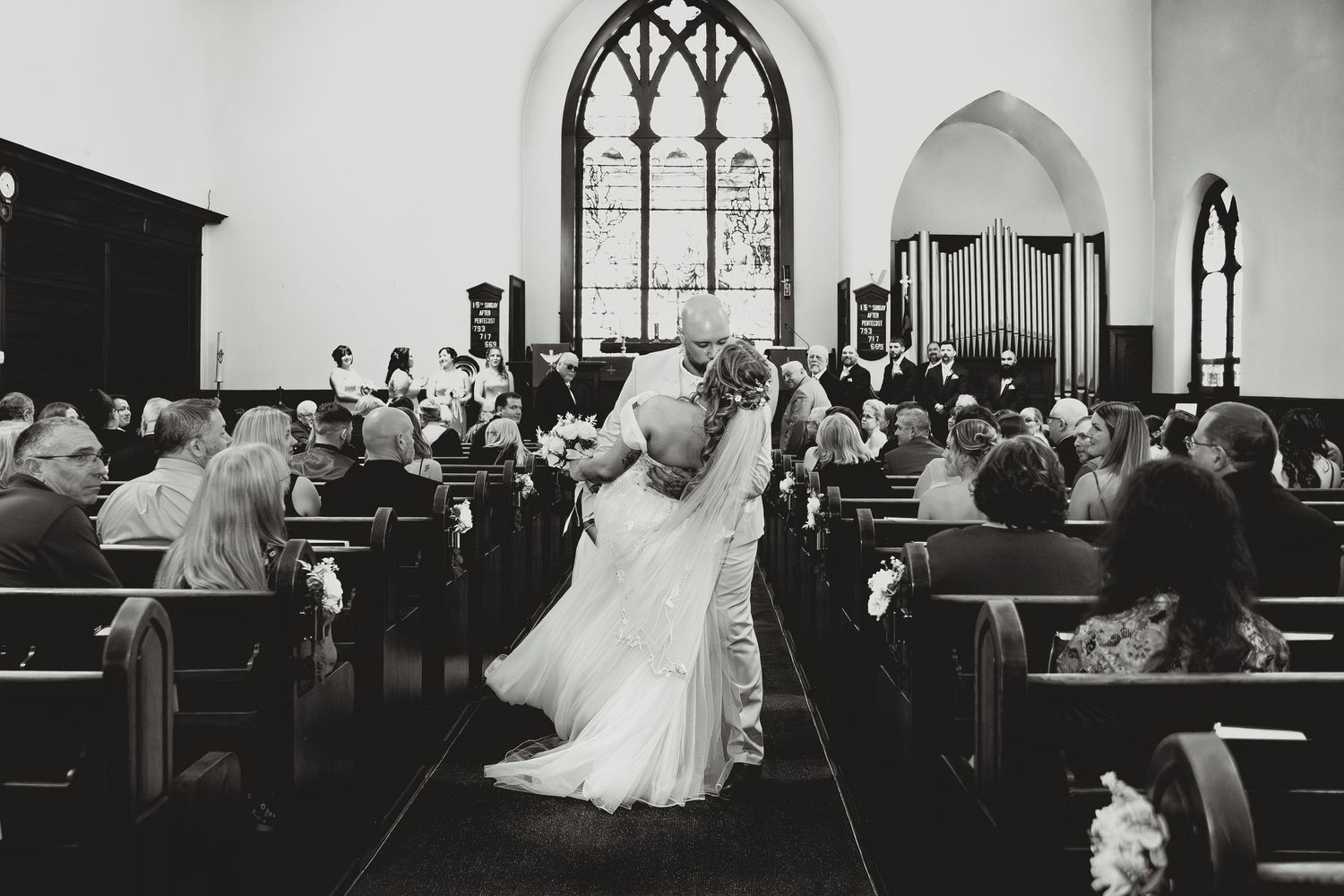 A black and white photograph of a couple dancing in the aisle of a church during a wedding ceremony.