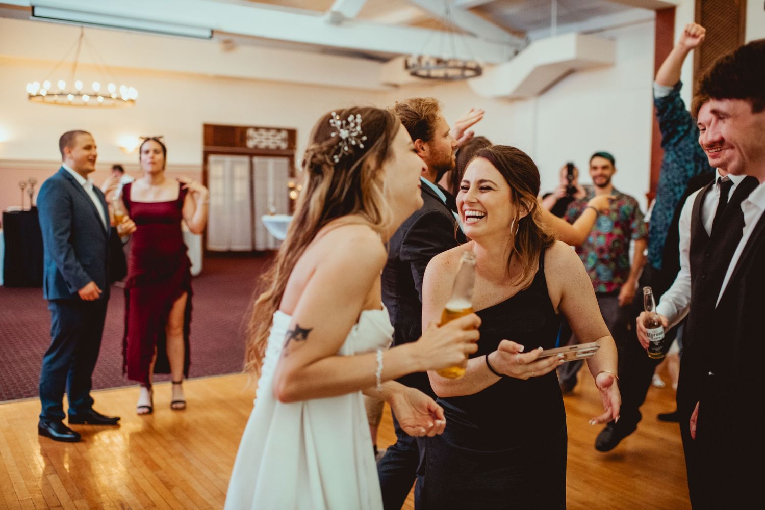 Wedding guests dancing and enjoying themselves on a wooden dance floor at an indoor venue.