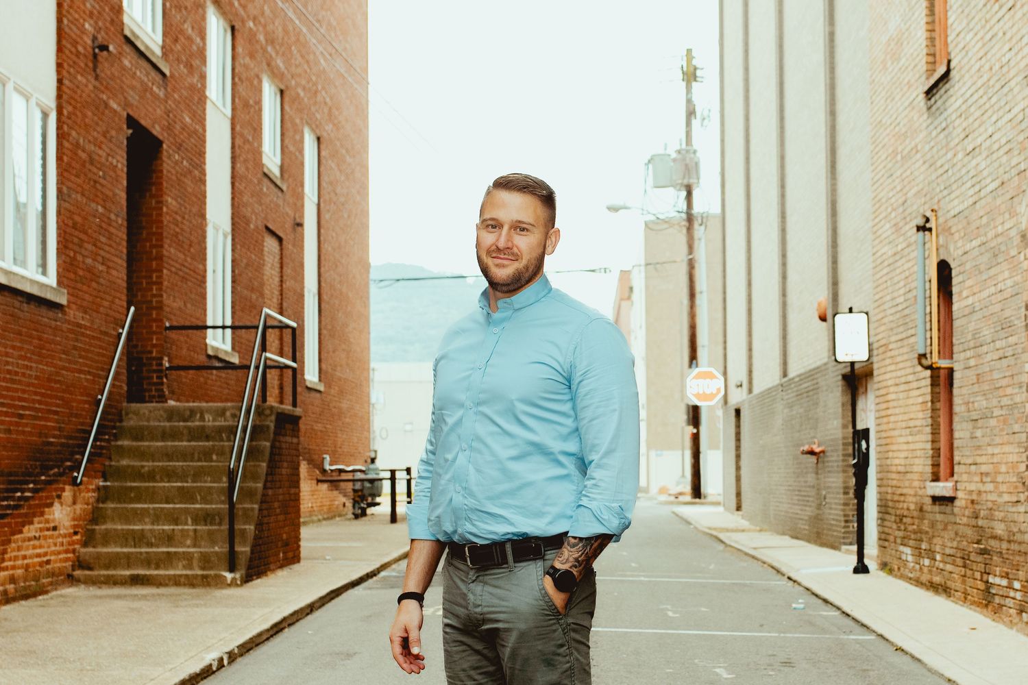 Someone in a light blue button-down shirt stands in an alley between brick buildings on a sunny day.