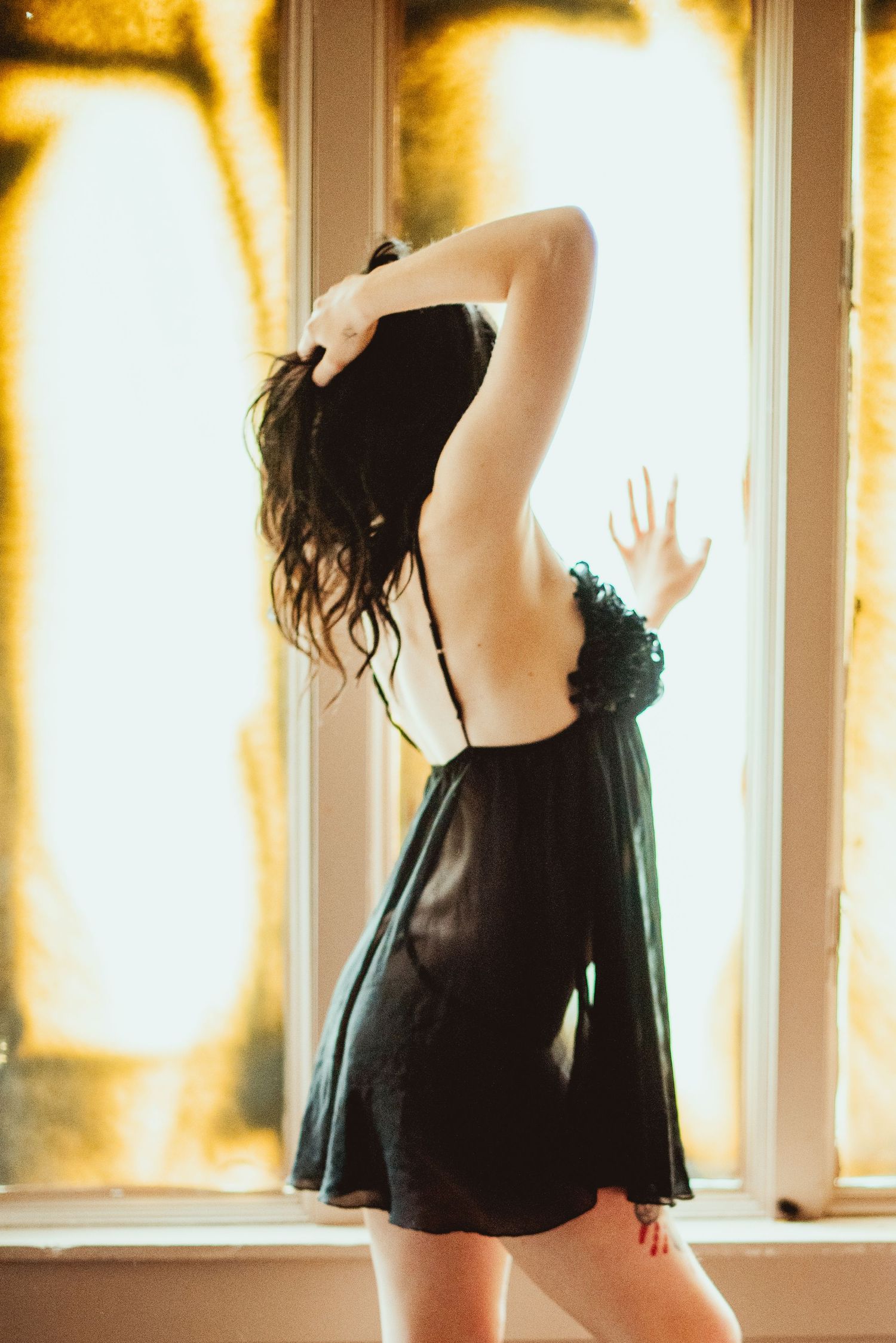 Silhouetted figure in black dress dances gracefully near sunlit windows creating a dreamy atmospheric scene.