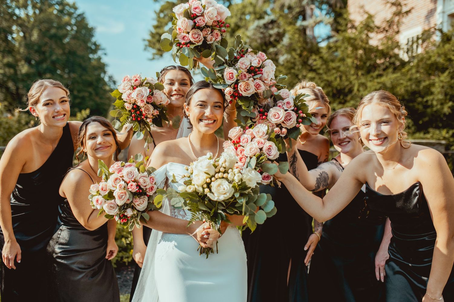 Wedding party posing outdoors with pink and white floral arrangements.