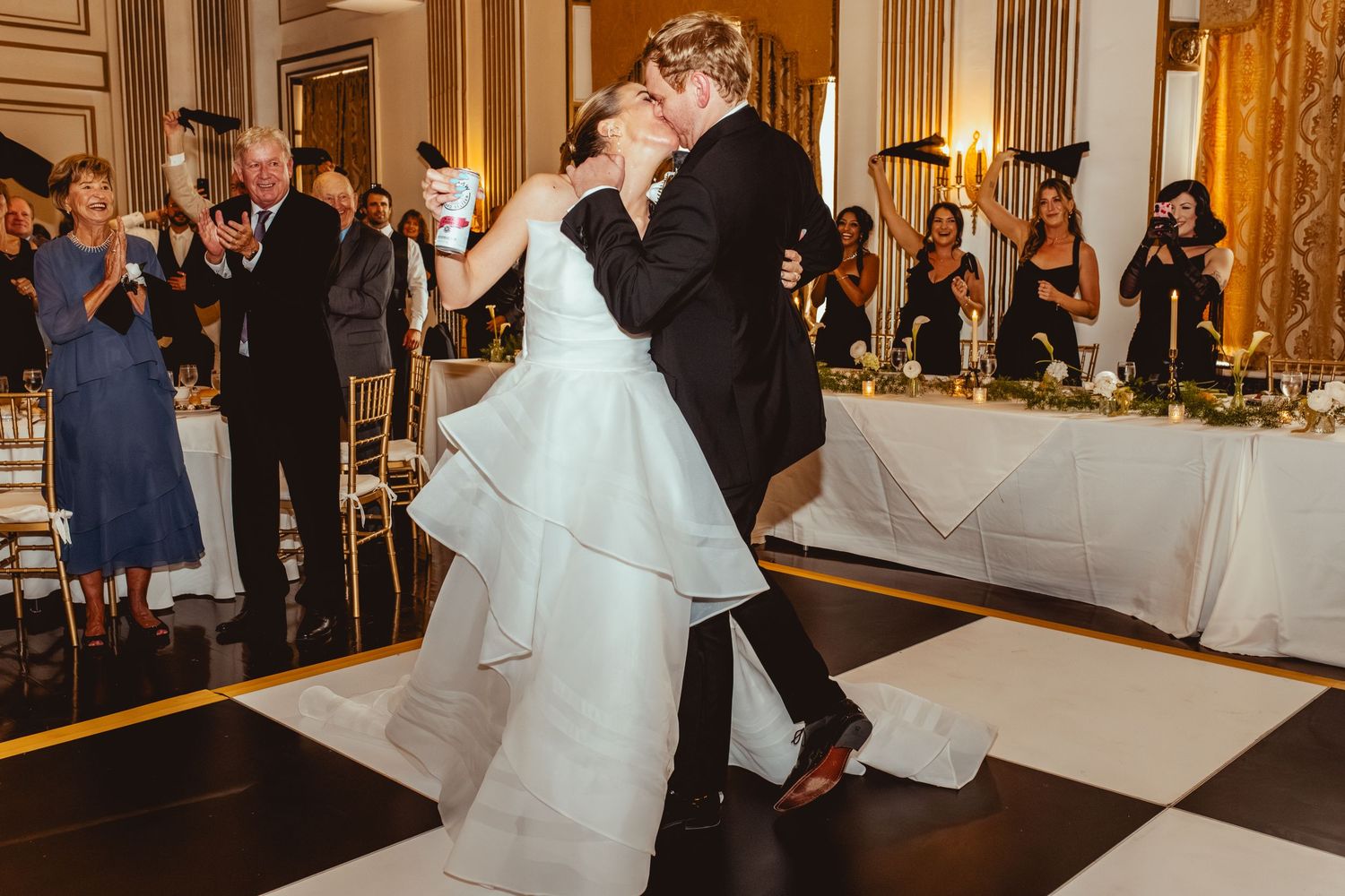 Wedding reception in an ornate ballroom with gold details and guests dancing.