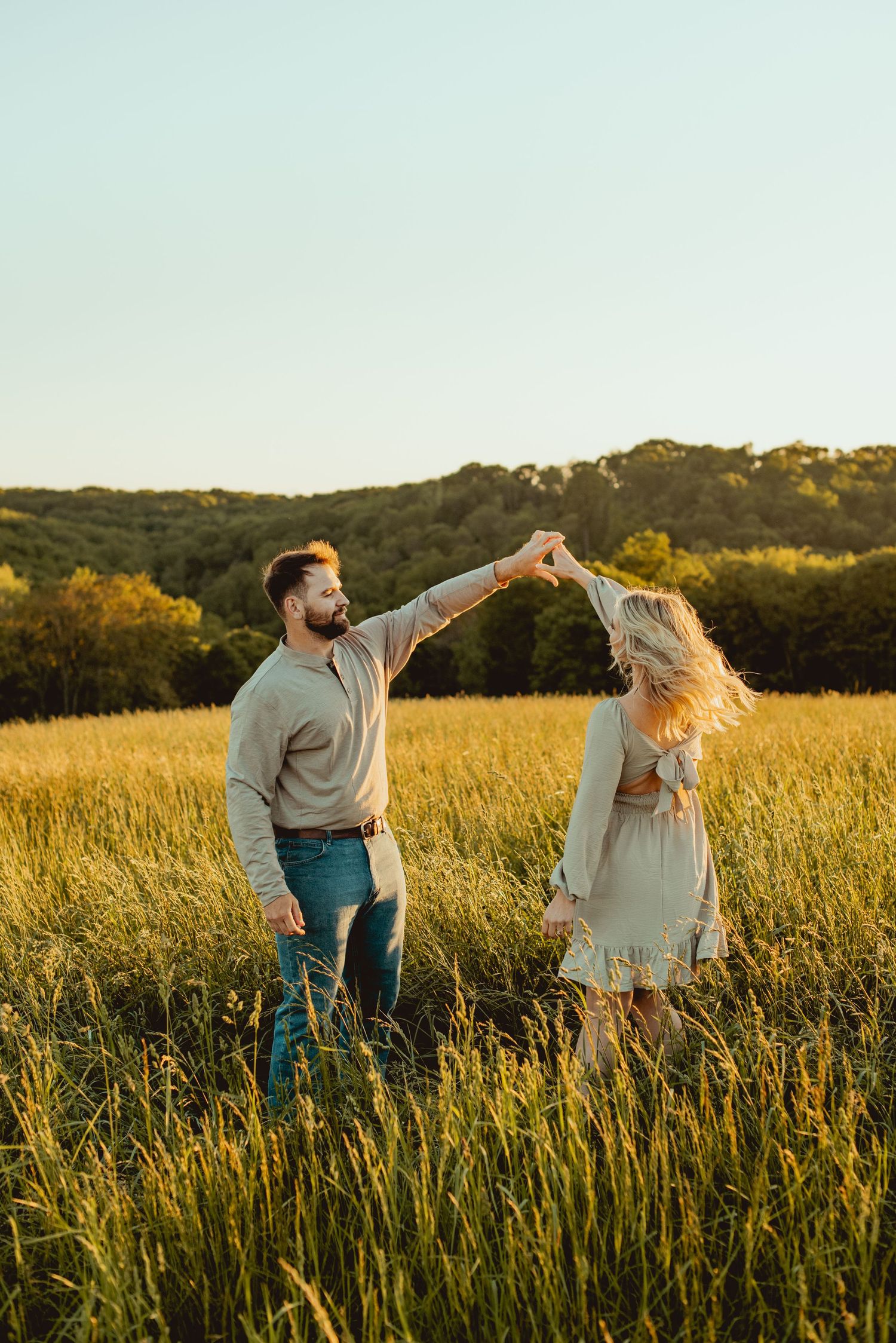 A couple dances playfully together in a golden field during sunset.