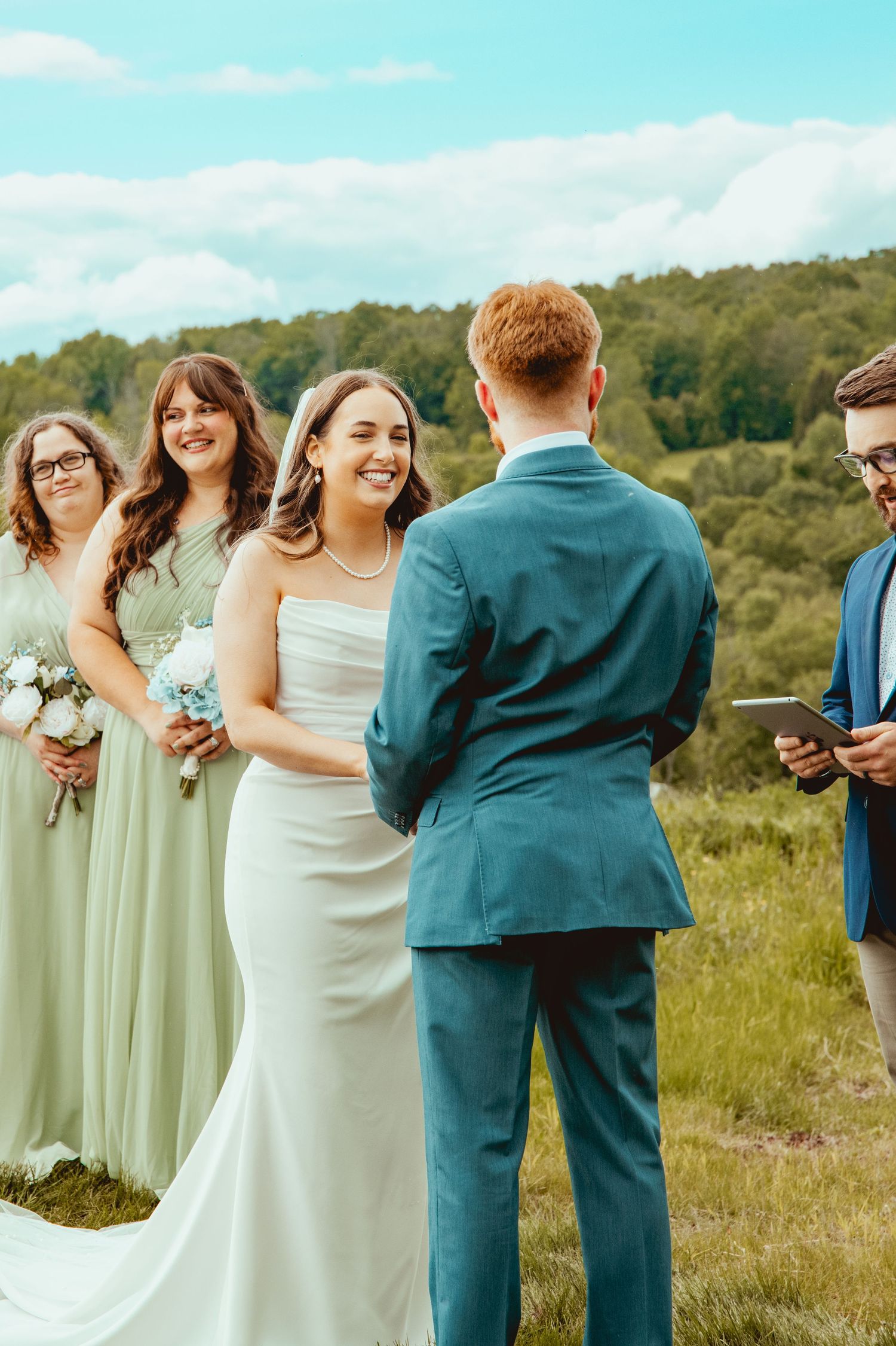 Wedding party in teal suits and mint green dresses posing in a grassy field.