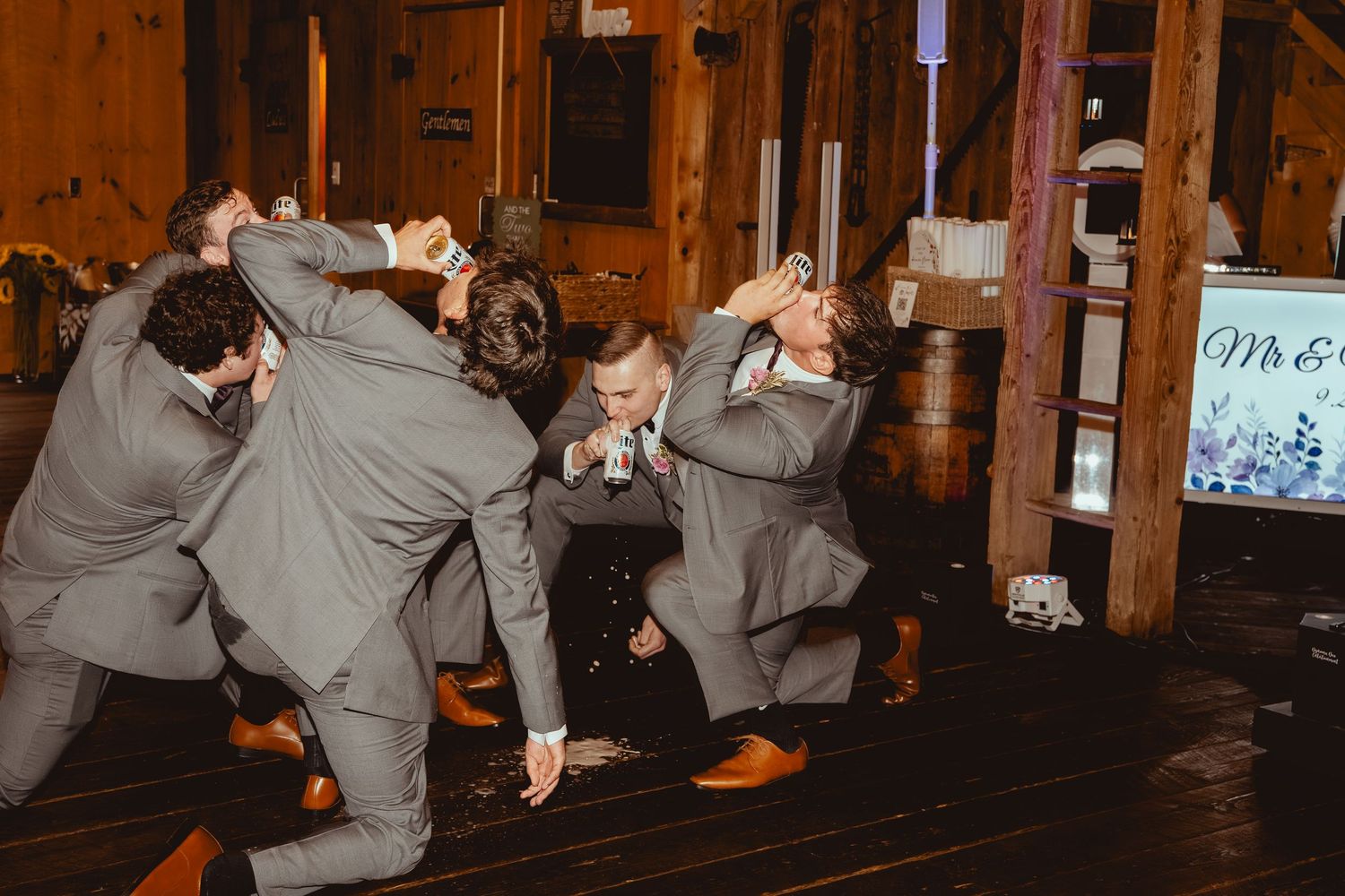 Wedding reception guests dancing and celebrating in a rustic wooden barn venue with warm lighting.