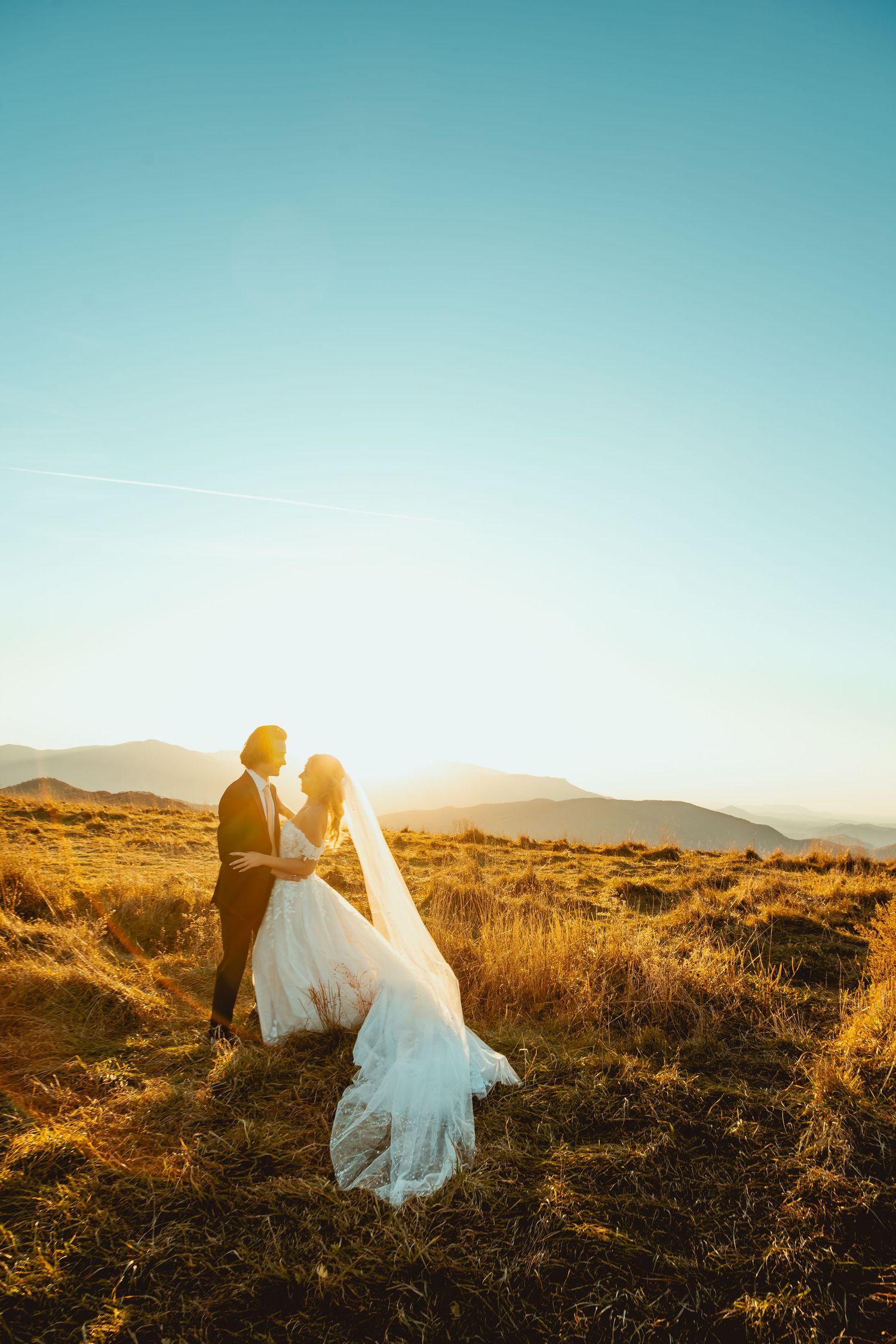 A bride and groom share an intimate moment during golden hour in a mountain setting.