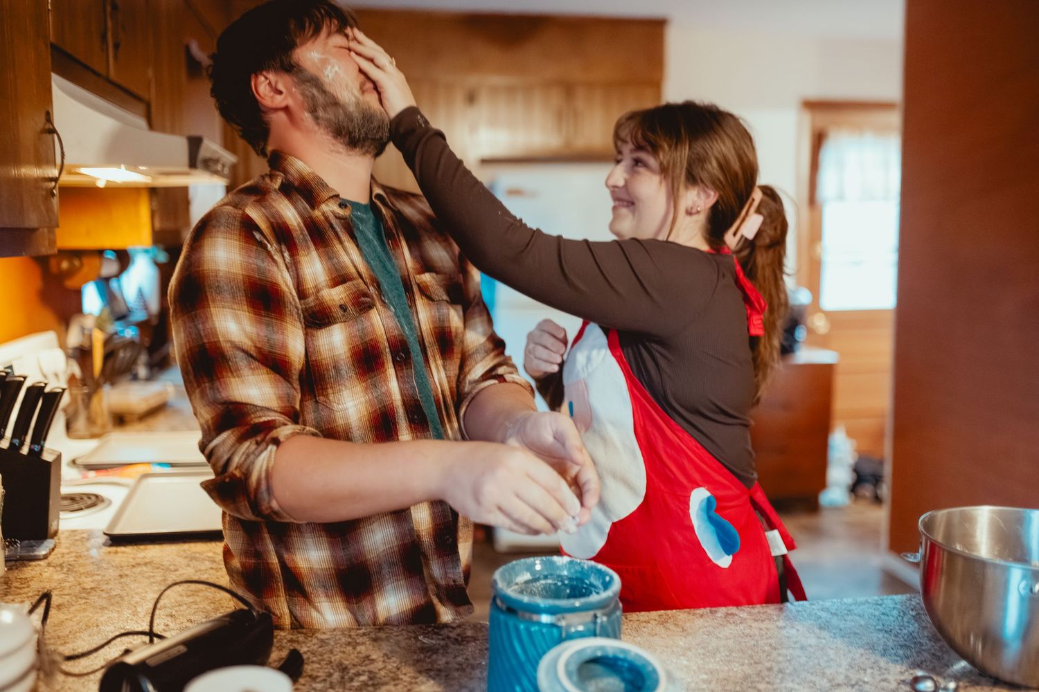 People gather in a cozy wooden cabin kitchen to prepare food together during a group cooking session.