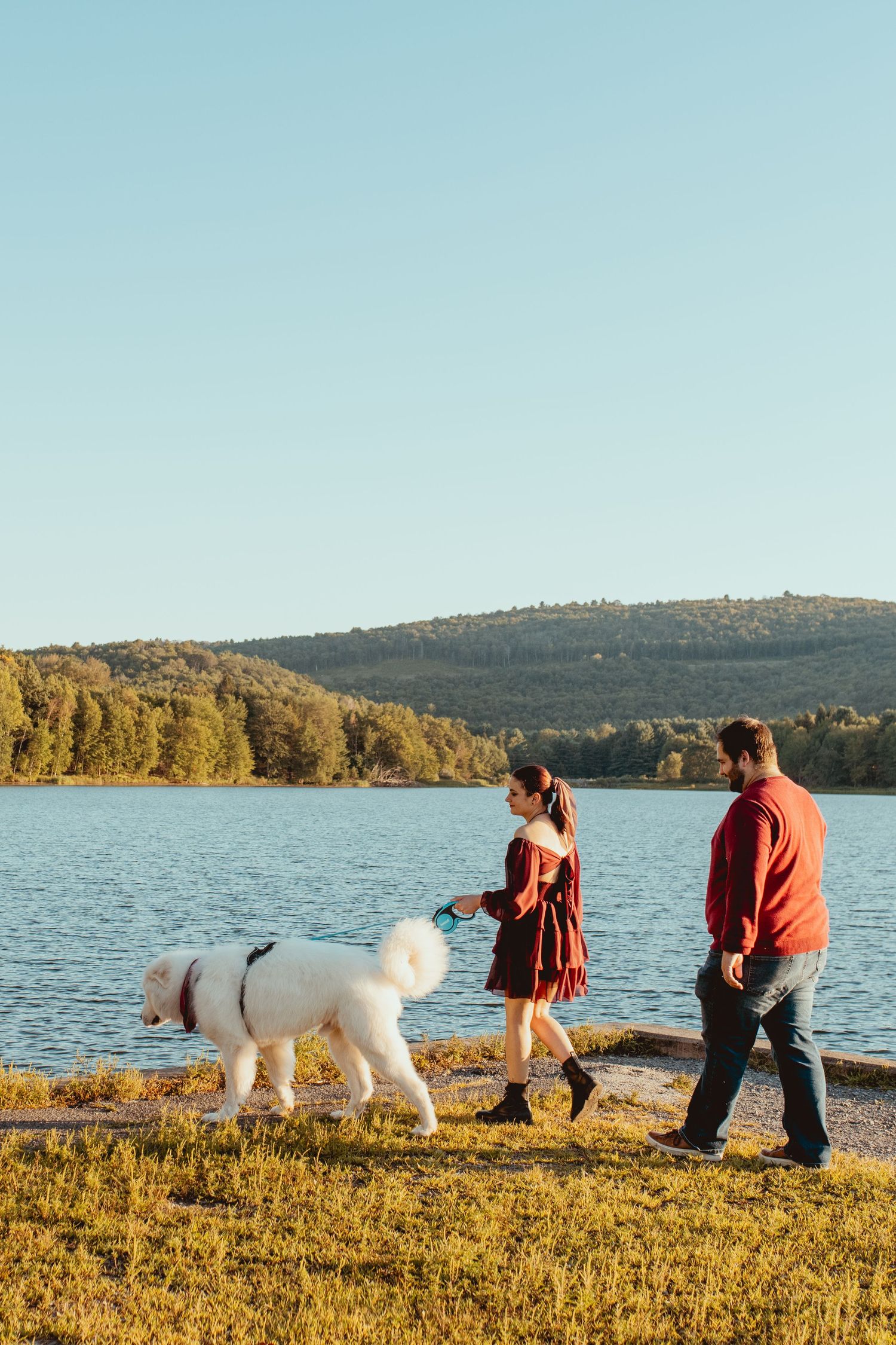 People walking with a large white dog along a scenic lakeside trail during golden hour.