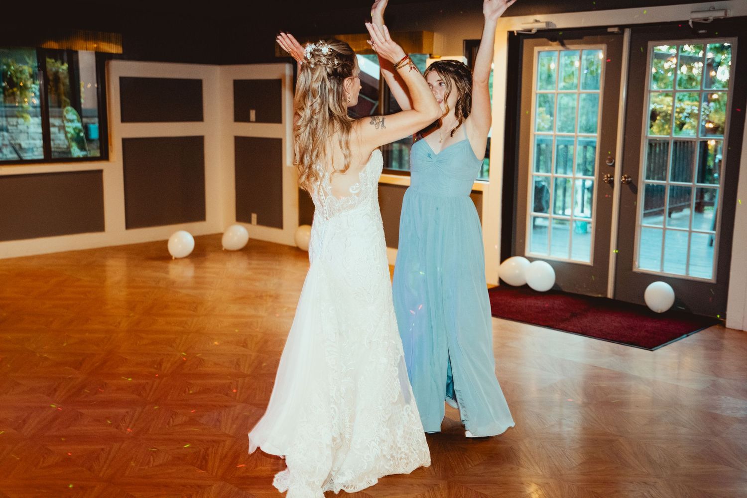 Wedding party members in blue and white dresses dance together on a wooden dance floor.