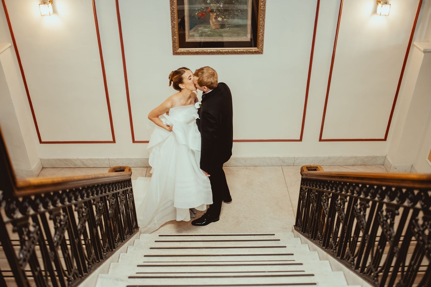 Wedding party posing on a grand white staircase with classic architectural details.