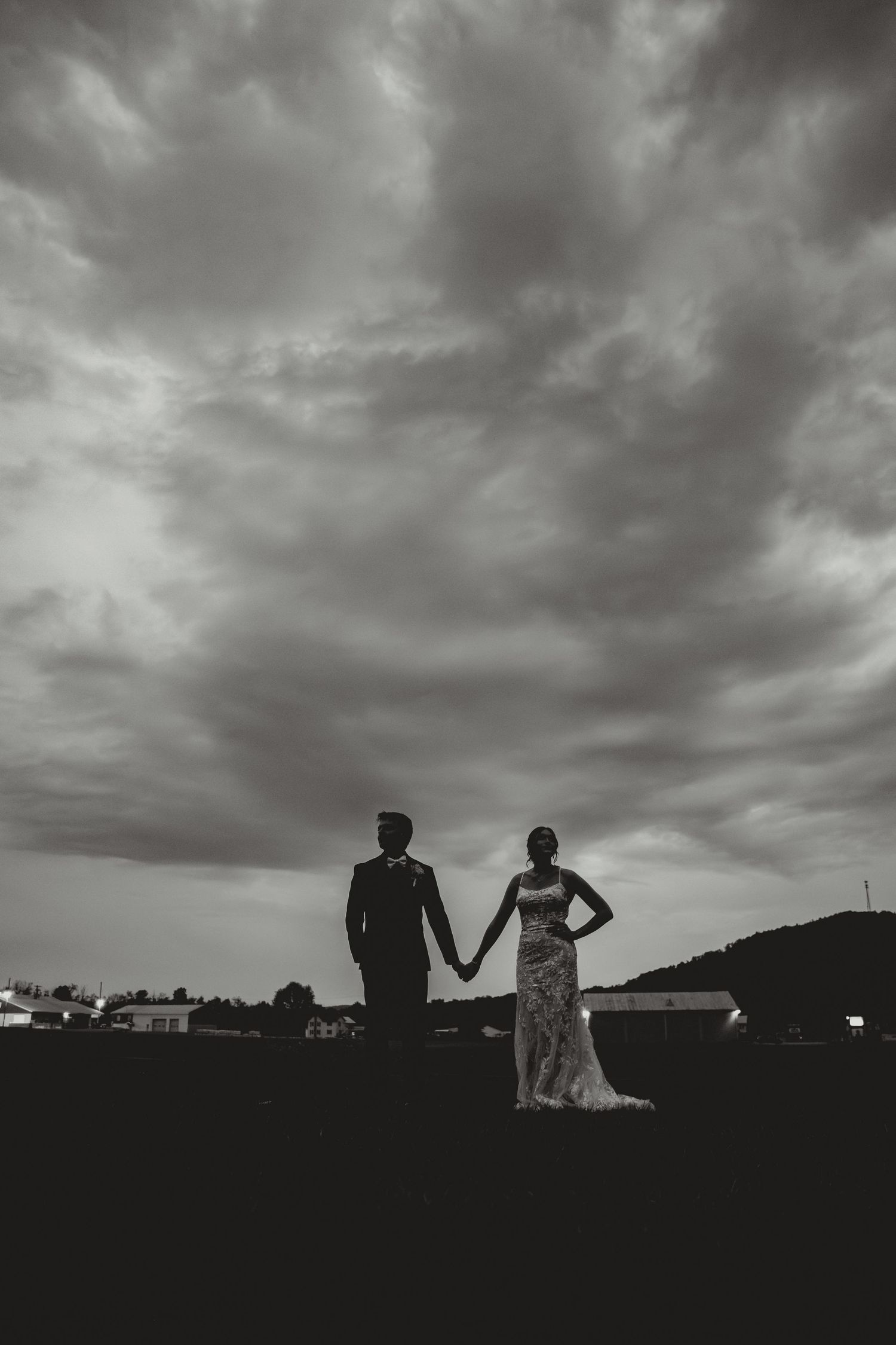 Dramatic black and white silhouettes against a moody cloudy sky during an outdoor wedding photoshoot.