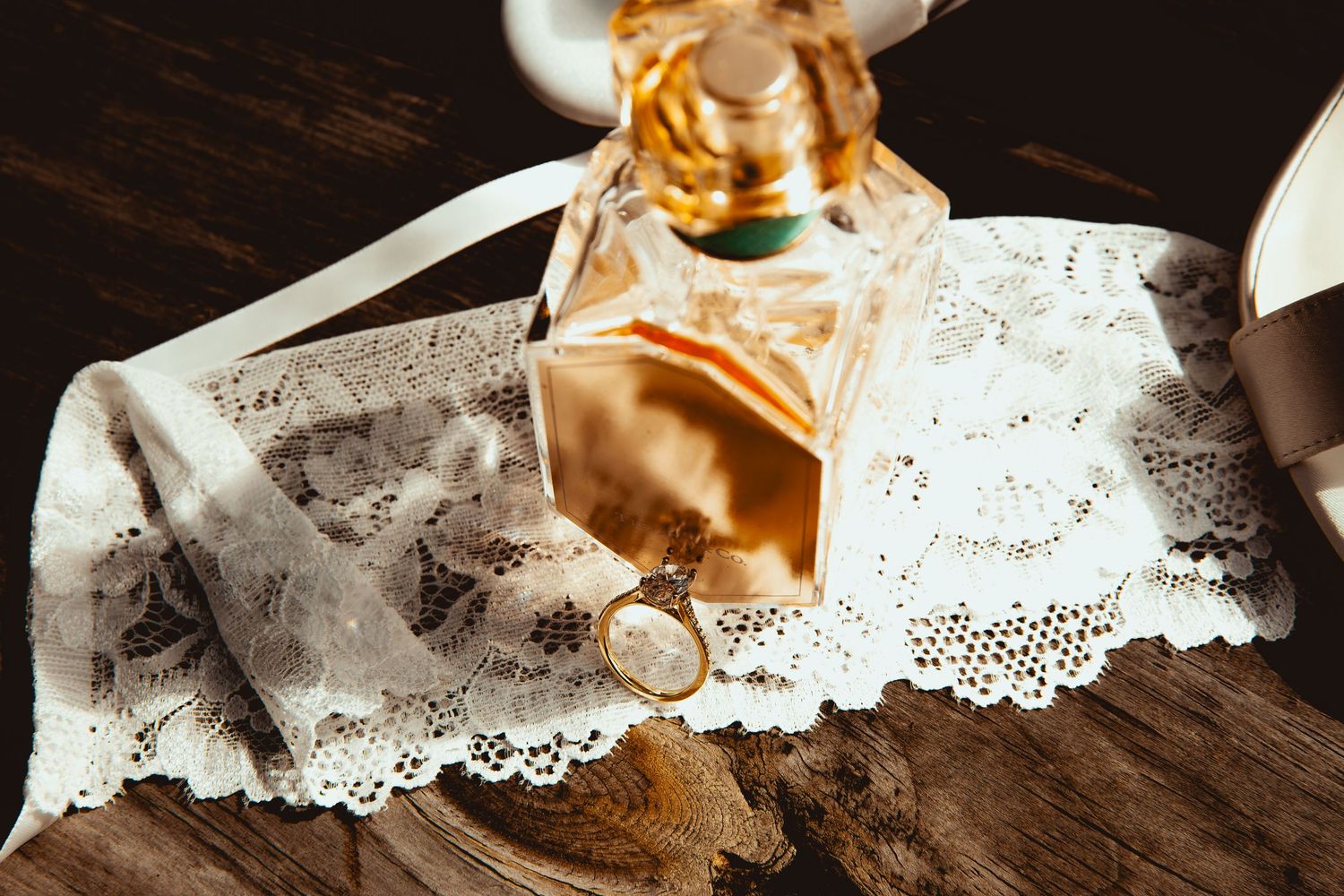 Delicate white lace and satin wedding details arranged on rustic wooden surface with warm lighting.