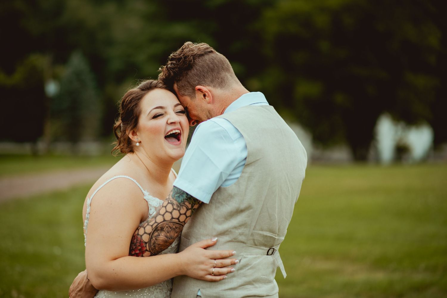 Joyful bride and groom sharing a laugh during an outdoor wedding portrait in a lush green park.