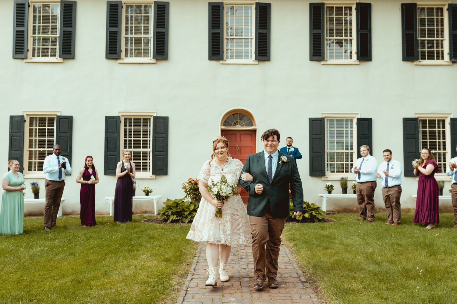 Wedding party gathered outside a historic white colonial building with black shuttered windows.