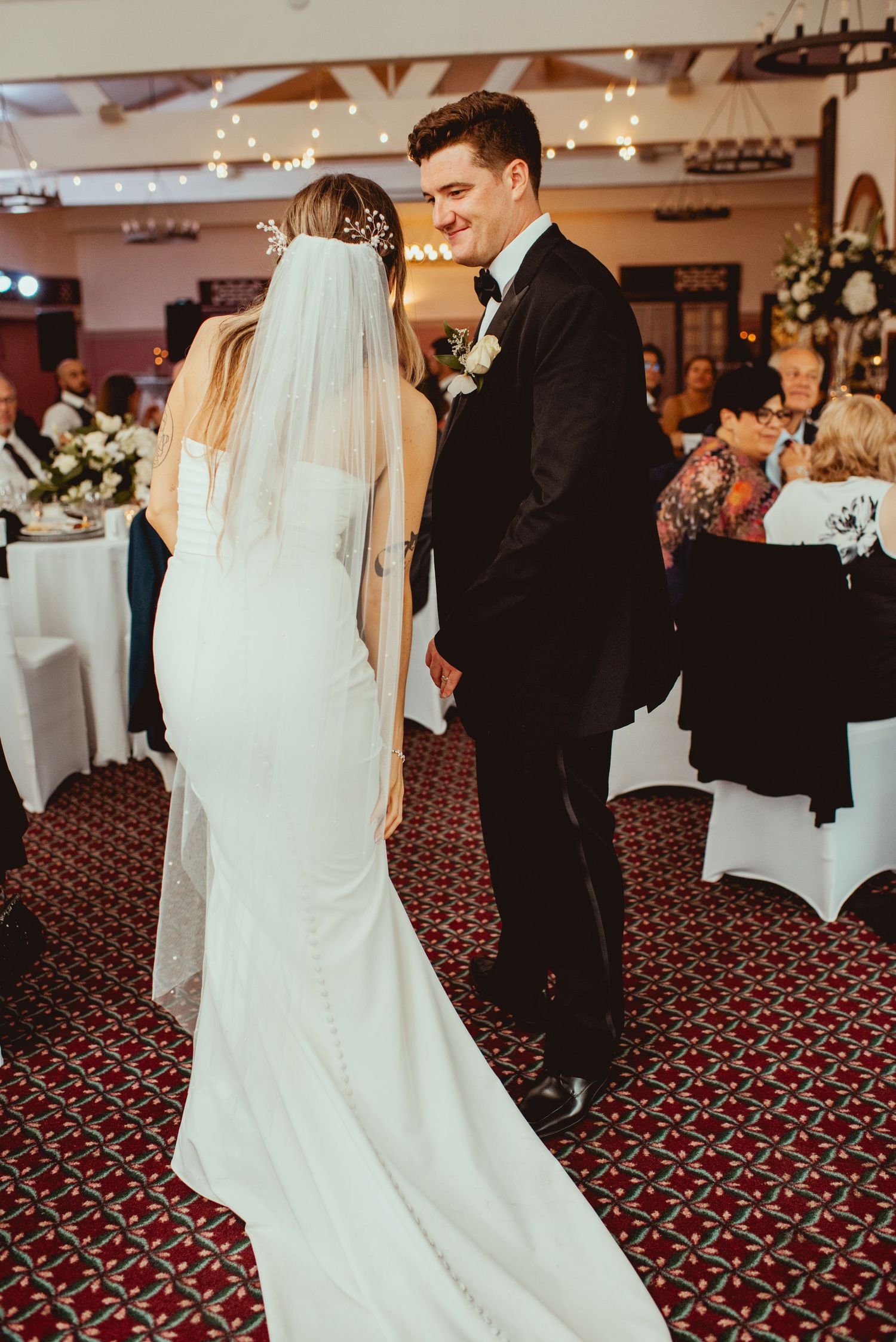 Wedding reception dance in a ballroom with red patterned carpet and string lights overhead.