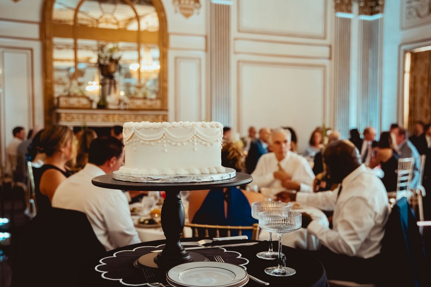 Wedding reception in an ornate ballroom with chandeliers and guests seated at decorated tables.