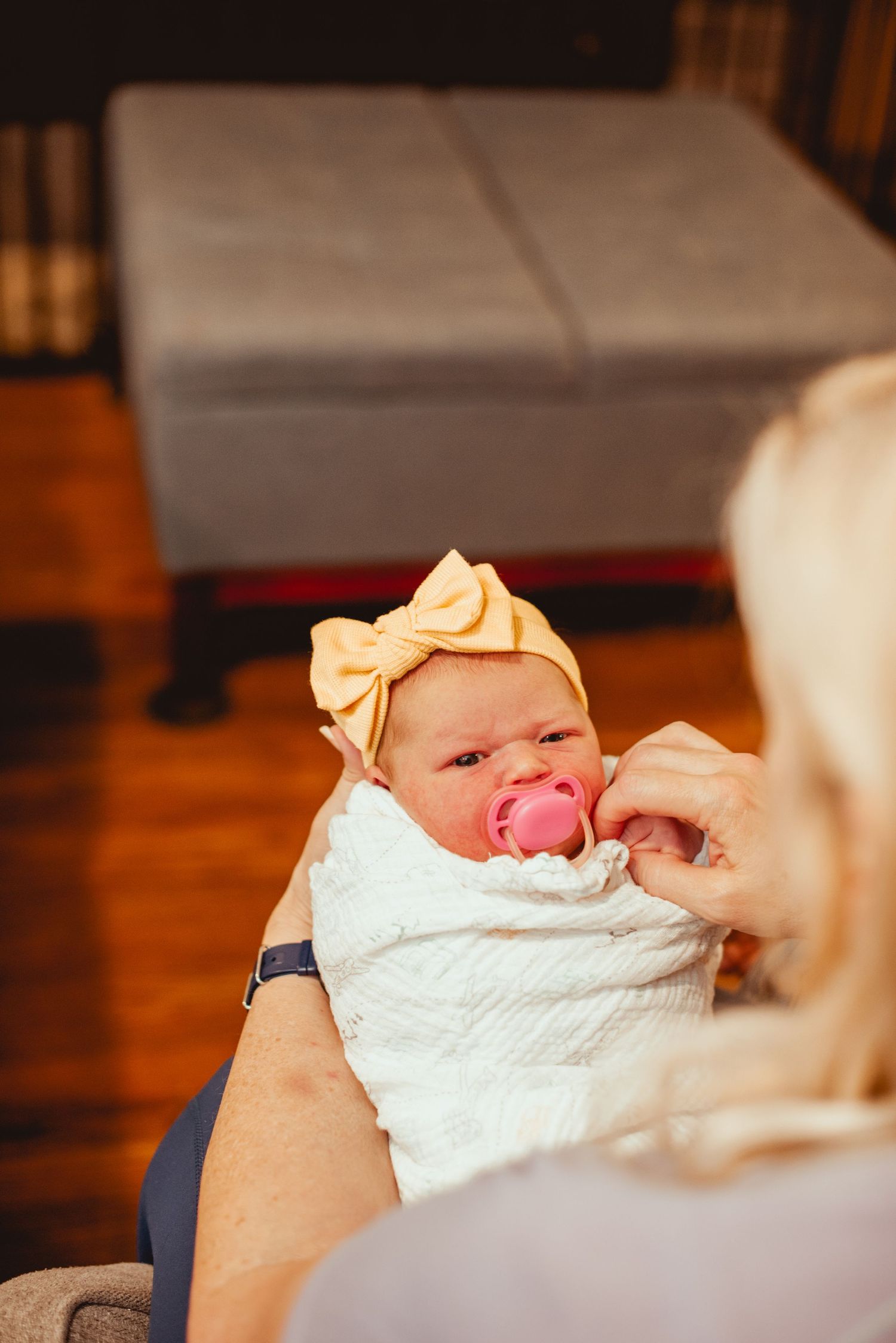 A sweet newborn wearing a yellow bow headband being cared for indoors.