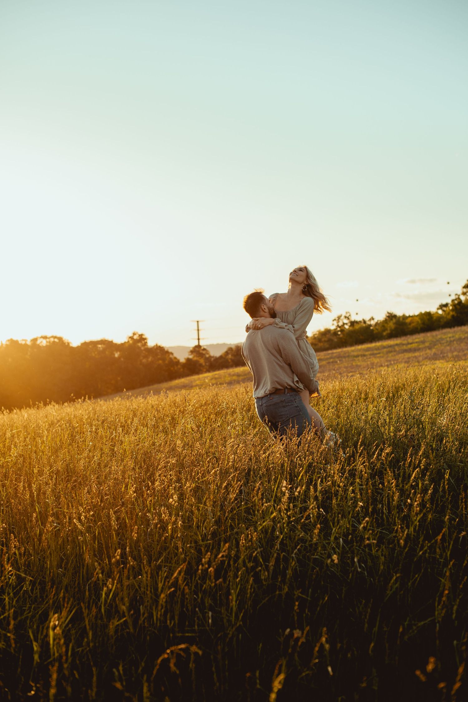 Romantic couple sits together in tall grass field during golden hour sunset.
