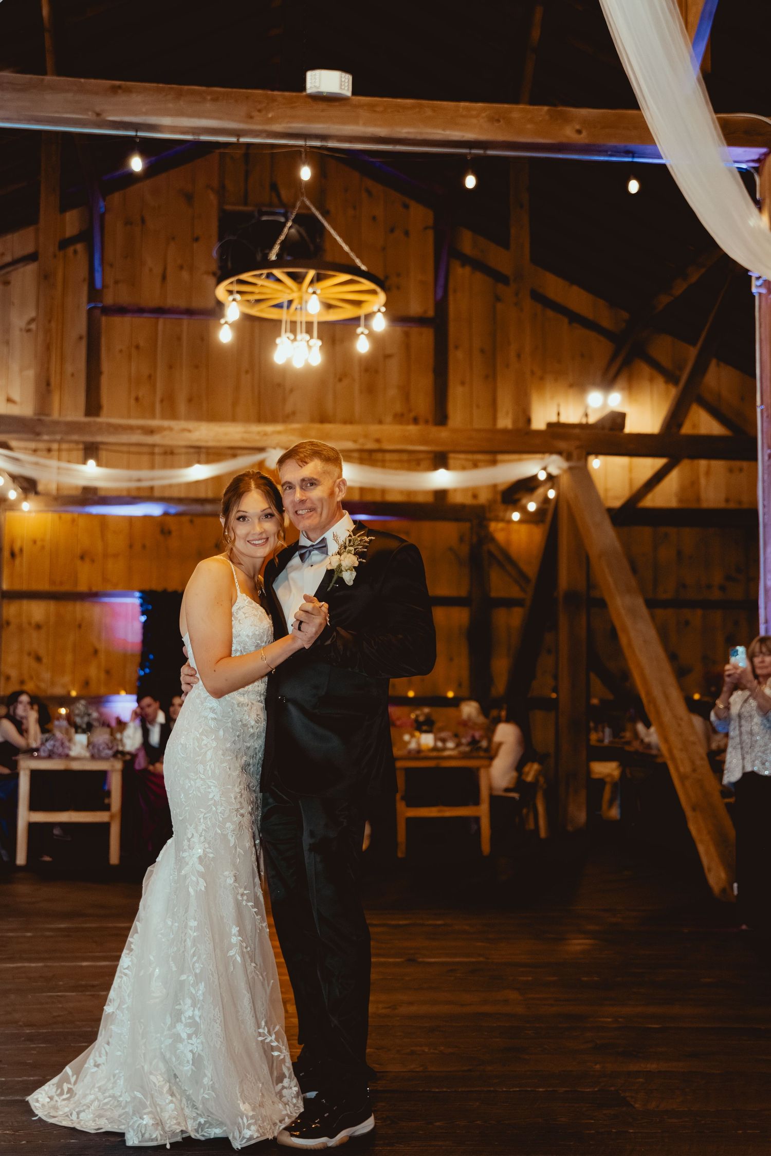 Wedding couple shares their first dance in a rustic barn venue with string lights overhead.