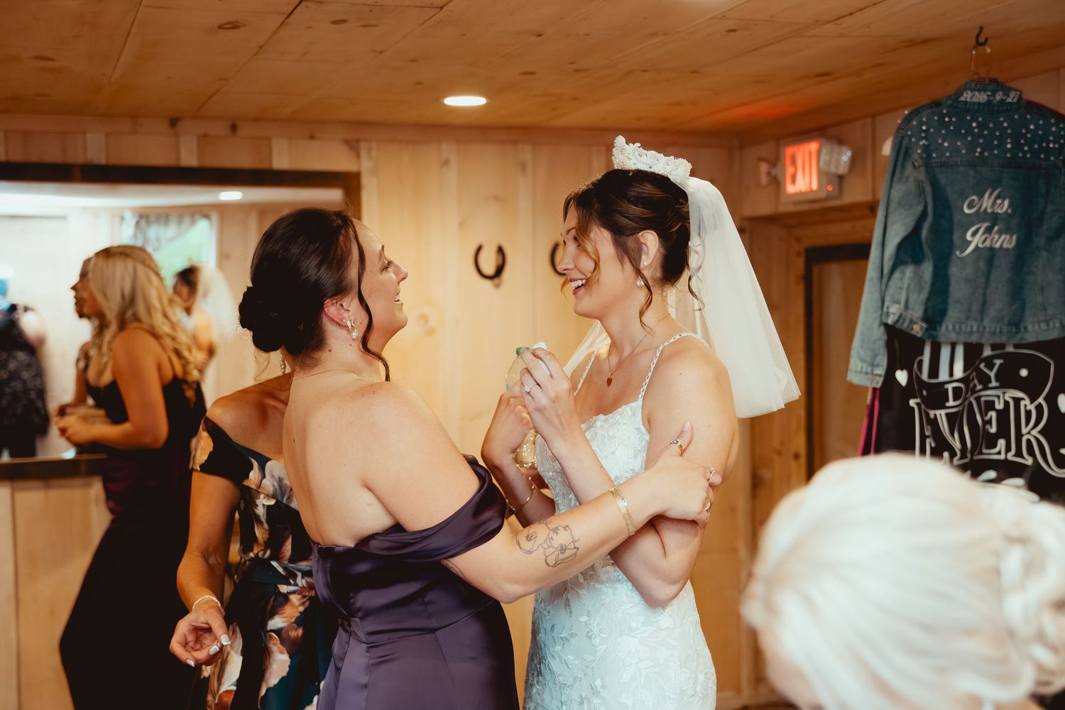 Two women in formal attire share an emotional moment during a wedding reception in a rustic indoor venue.
