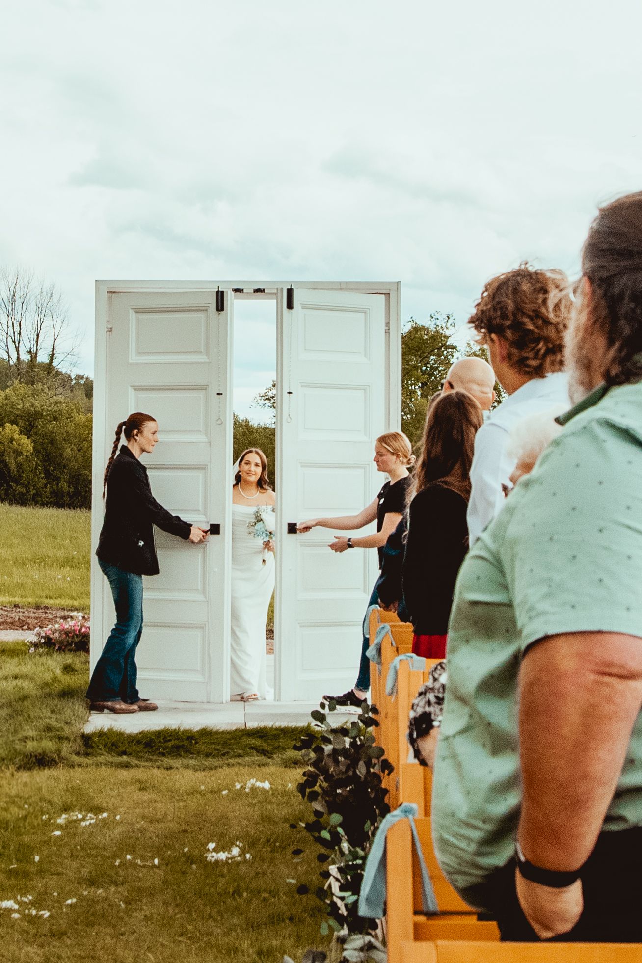 Unique wedding ceremony setup featuring white doors as a backdrop in an outdoor field setting.