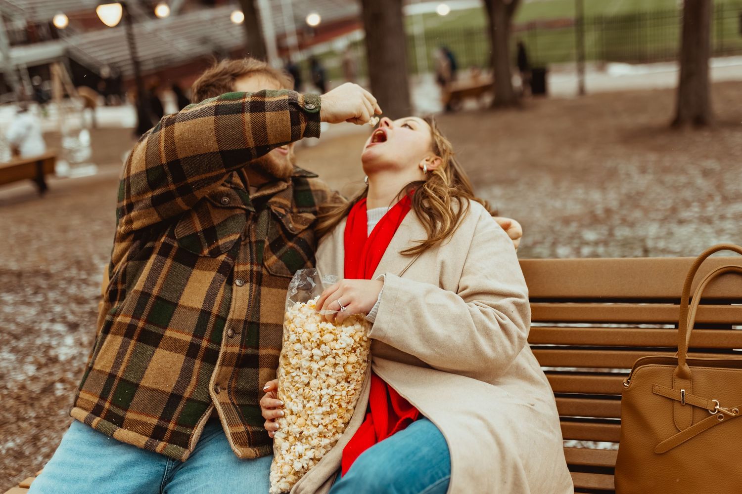 Romantic couple sharing popcorn while sitting on wooden bench in autumn park during golden hour.
