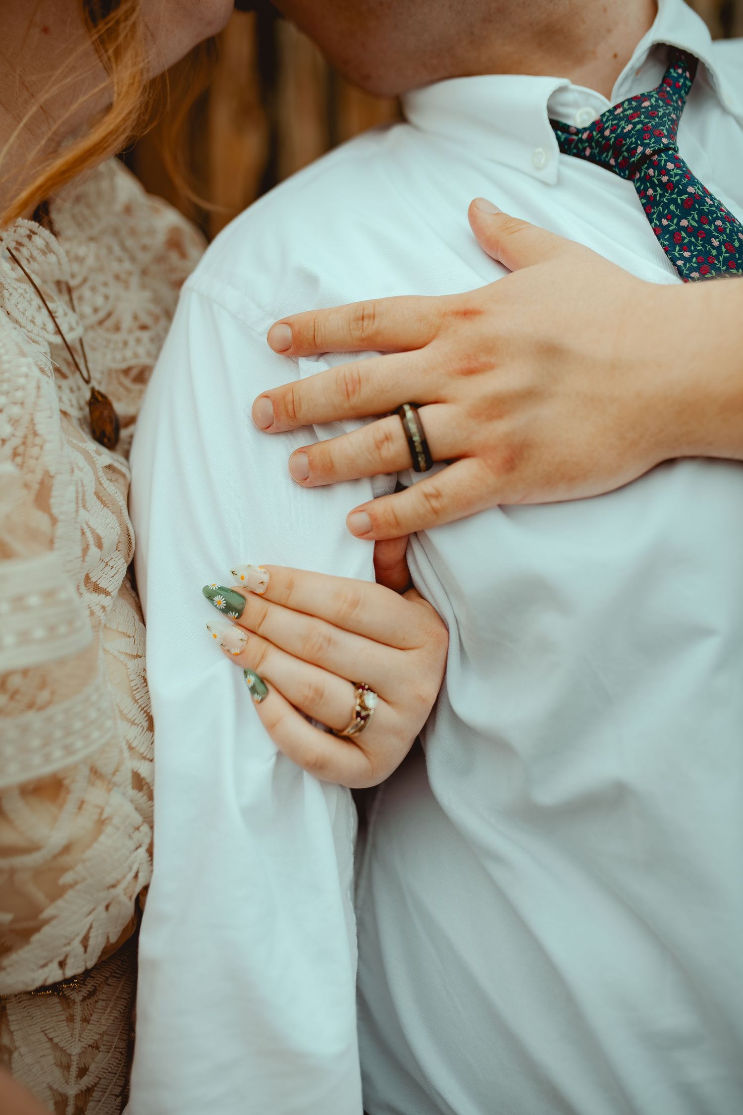 Close-up of hands displaying wedding rings against white formal attire with delicate details.