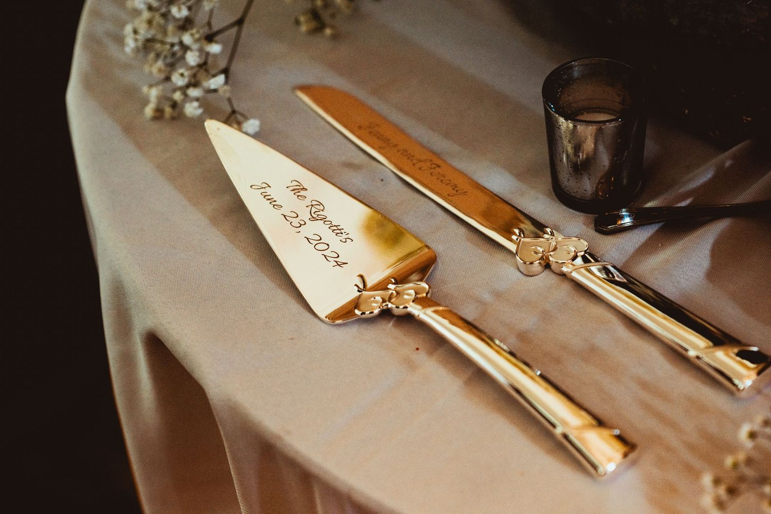 Elegant gold-handled wedding cake serving set displayed on champagne colored tablecloth.
