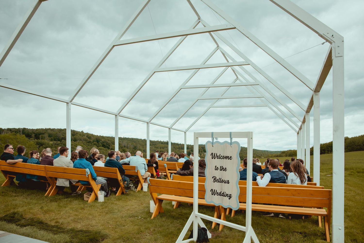 White wedding tent setup with wooden benches for guests in an outdoor field setting.