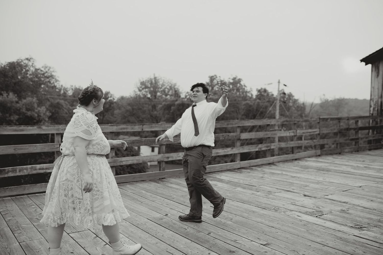 A joyful couple dances together on a wooden deck in black and white.