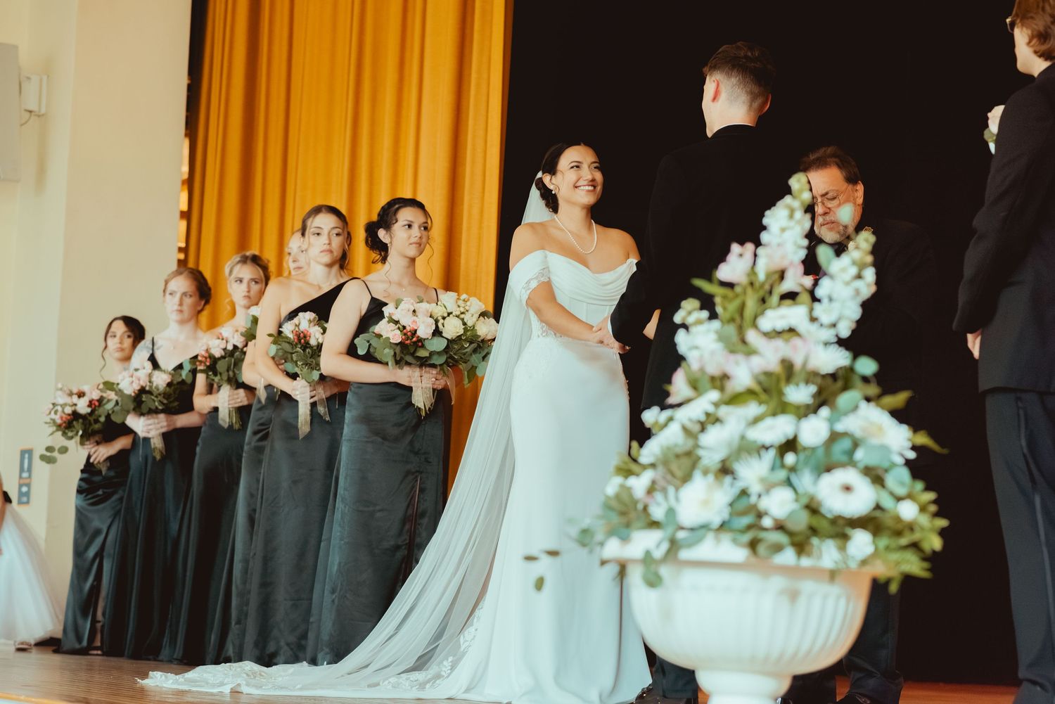 Wedding ceremony with bridesmaids in black dresses and white floral arrangements.