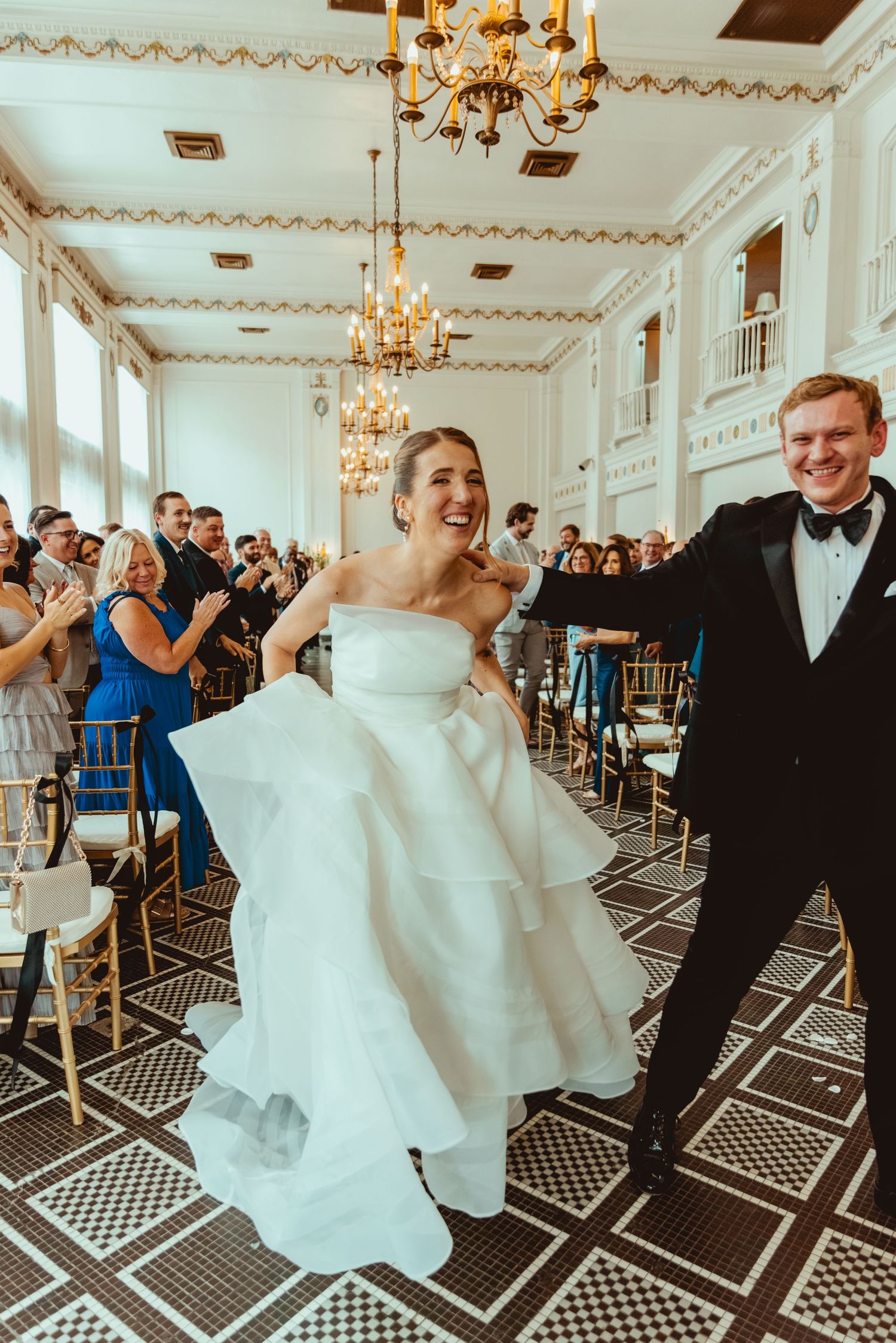 Wedding couple dances and celebrates on geometric patterned floor under crystal chandeliers.