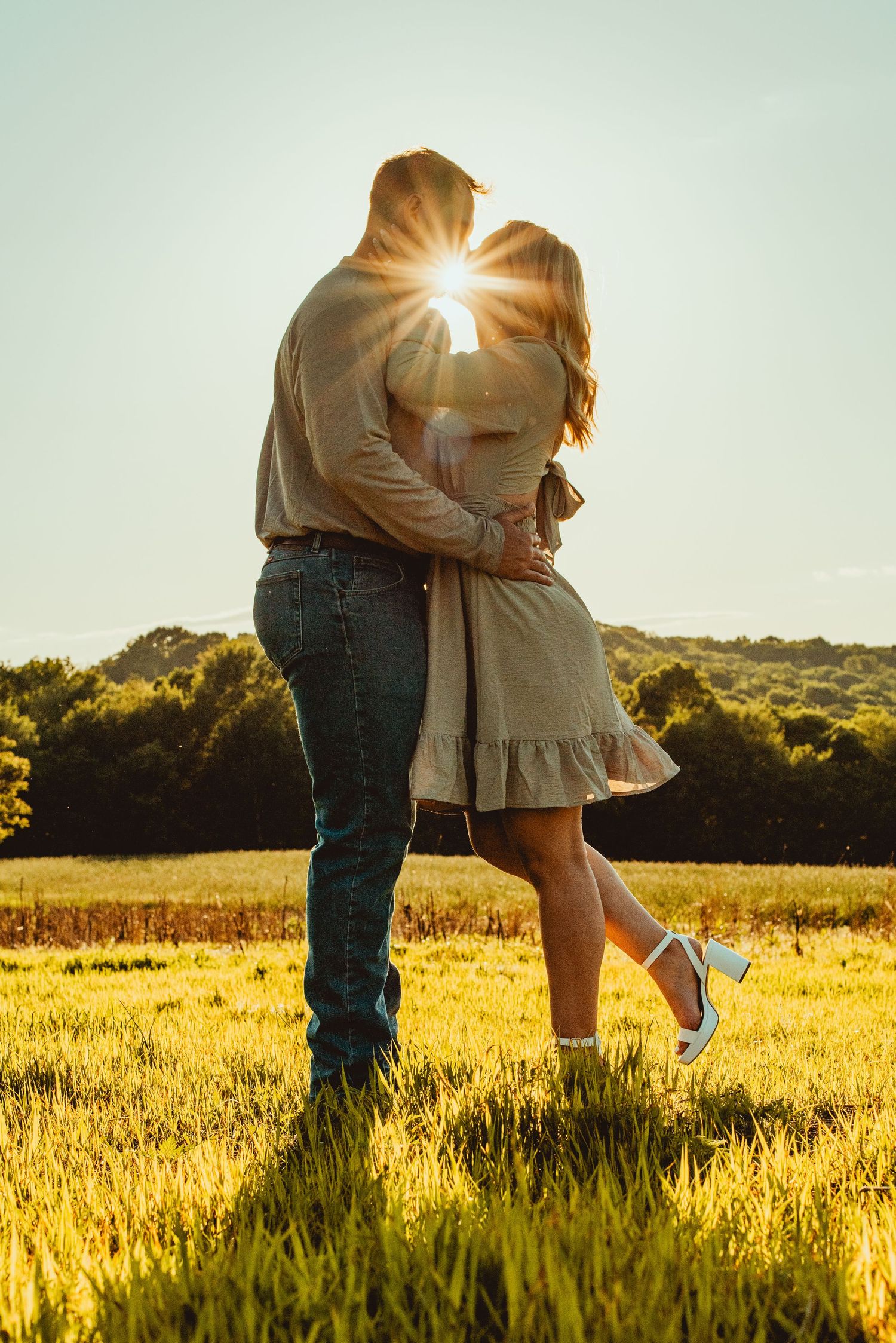 Couple embraces in golden sunlit field during sunset creating romantic silhouette against warm sky.