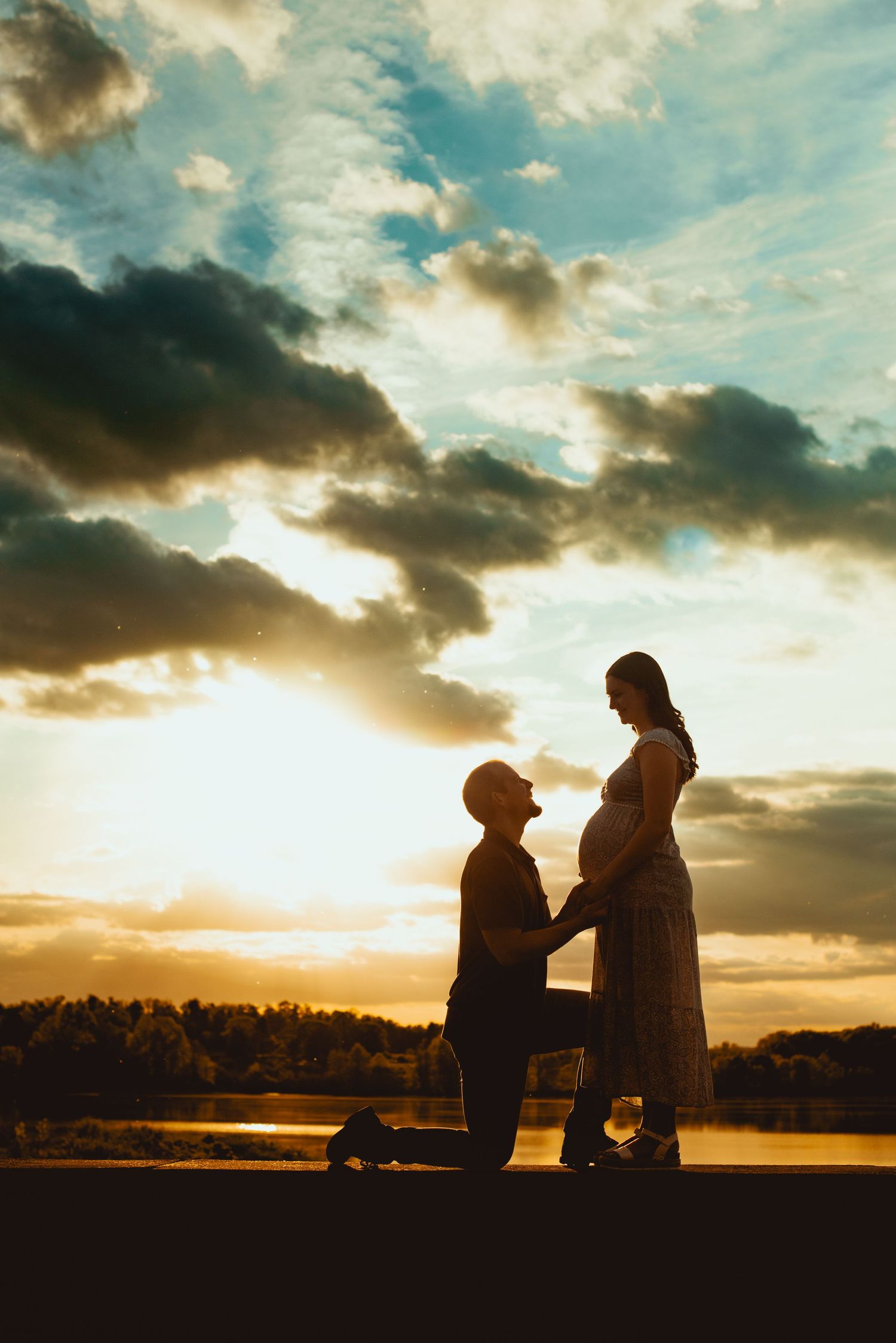 Silhouettes of two people share an intimate moment against a golden sunset sky over a tranquil lake.