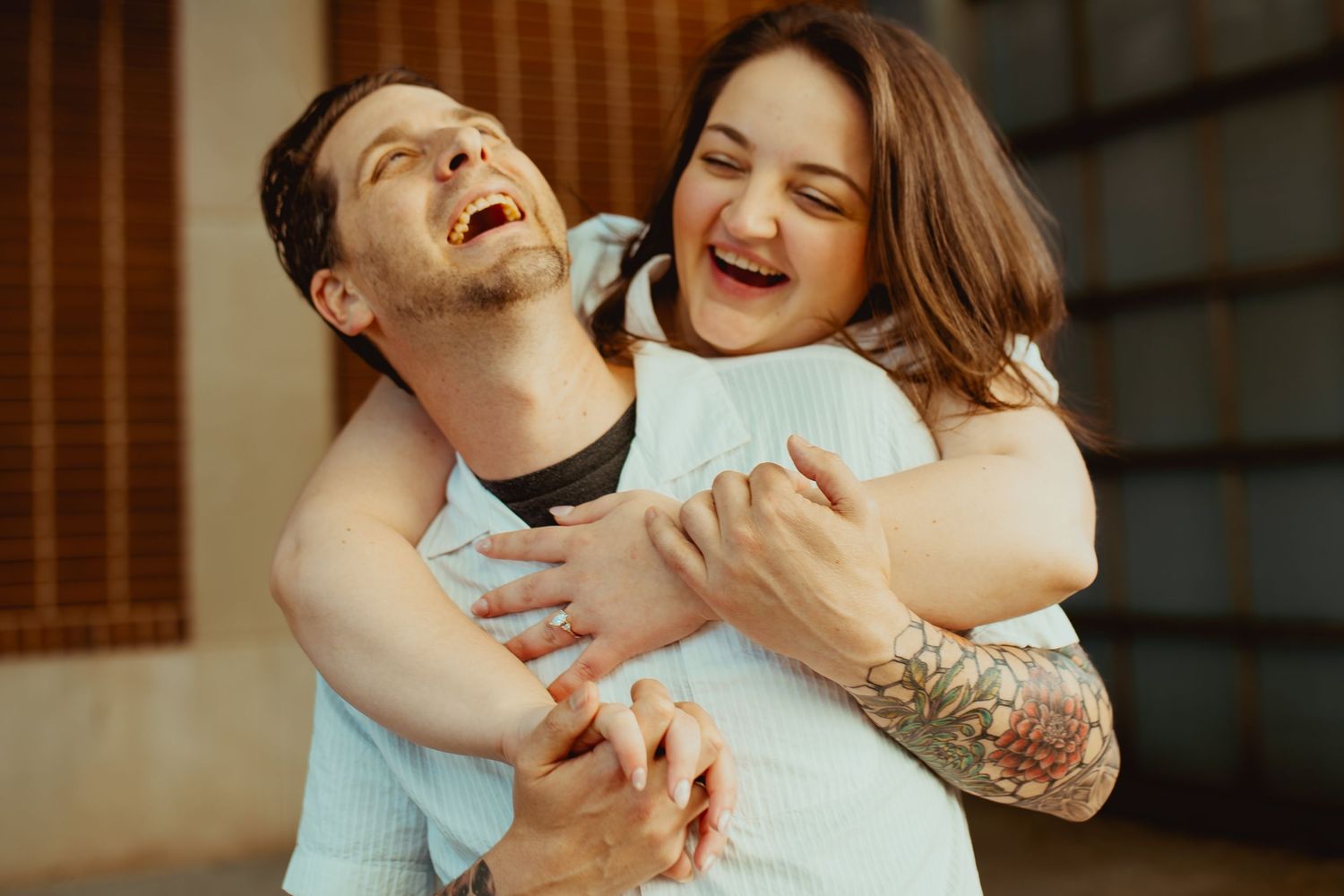 A laughing couple sharing a joyful hug, the man with a tattoo embracing a smiling woman in a warm, candid moment.