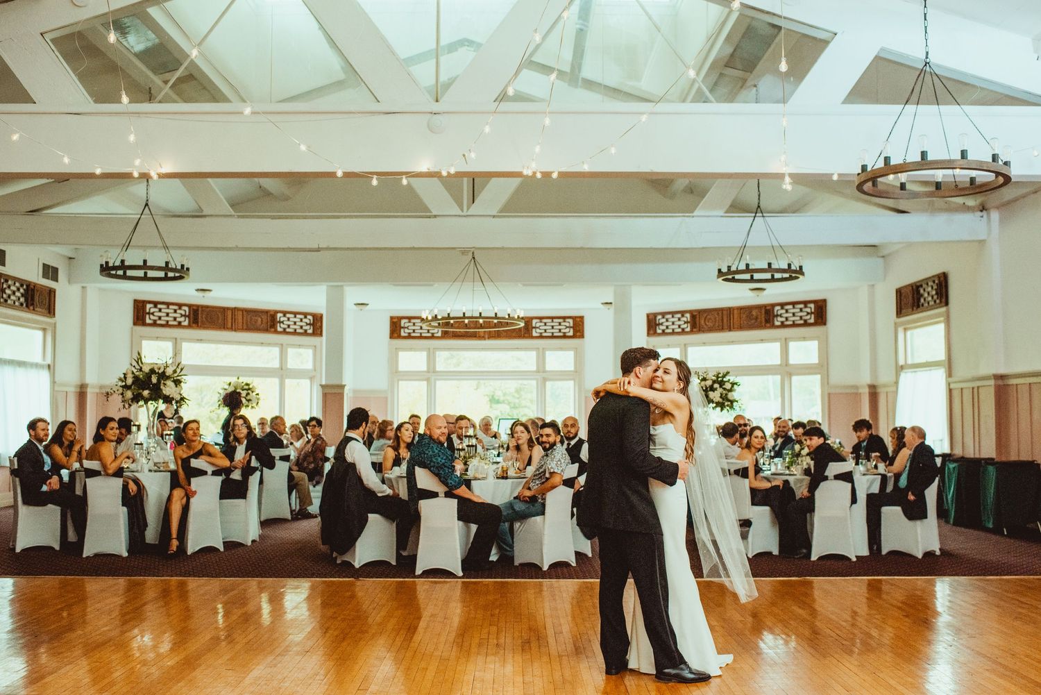 Panoramic view of an elegant white ballroom with chandeliers and hardwood floors.