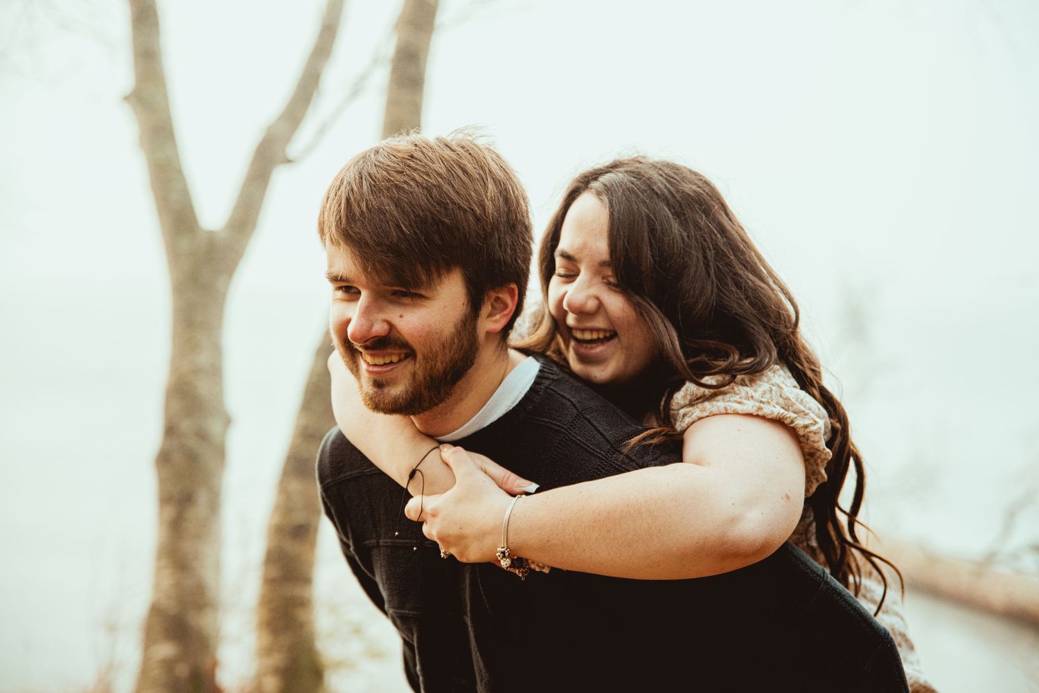 Happy couple embracing and laughing together during outdoor photo session in natural lighting.