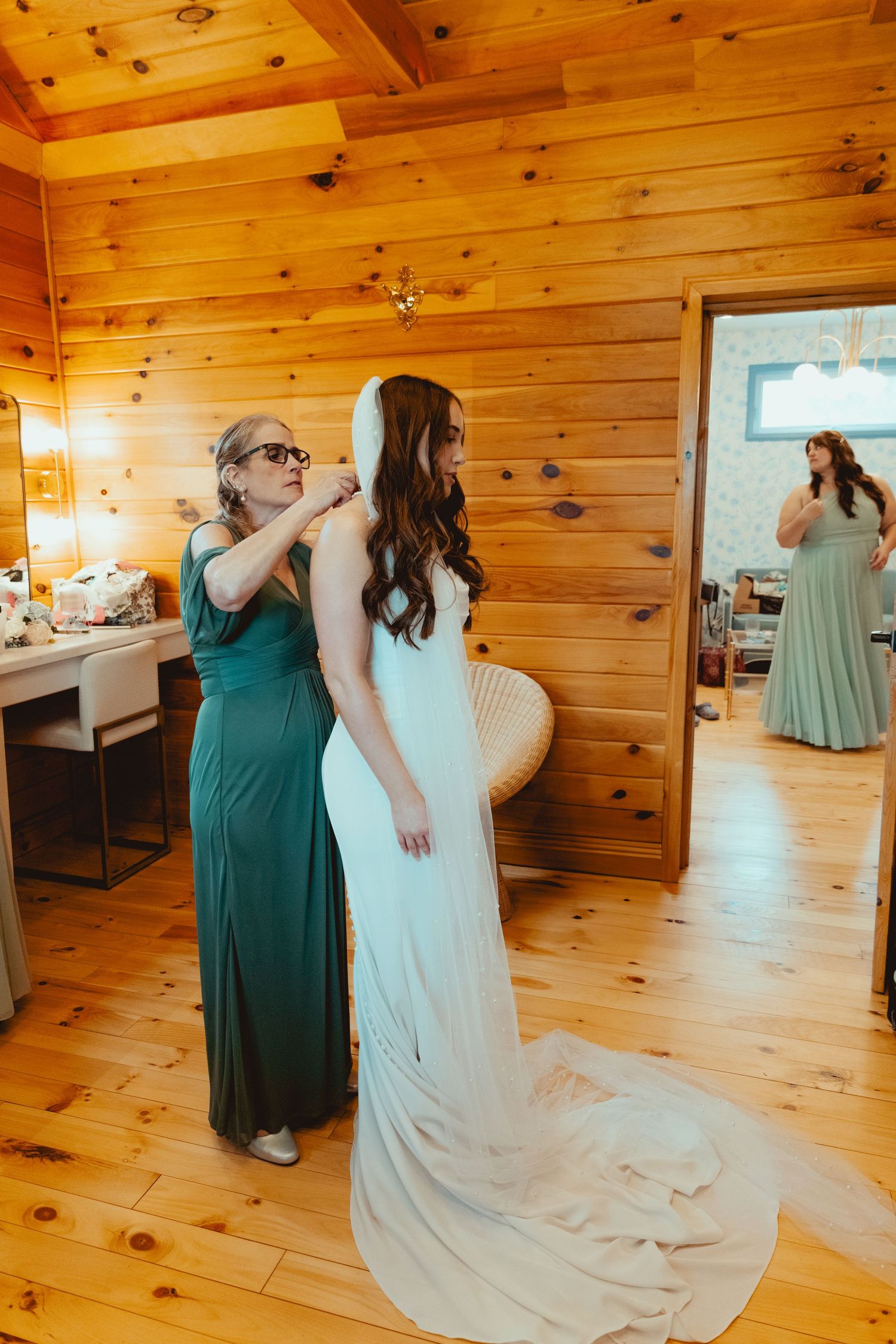 Final dress adjustments being made in a warm wooden cabin with mirrors and natural lighting.