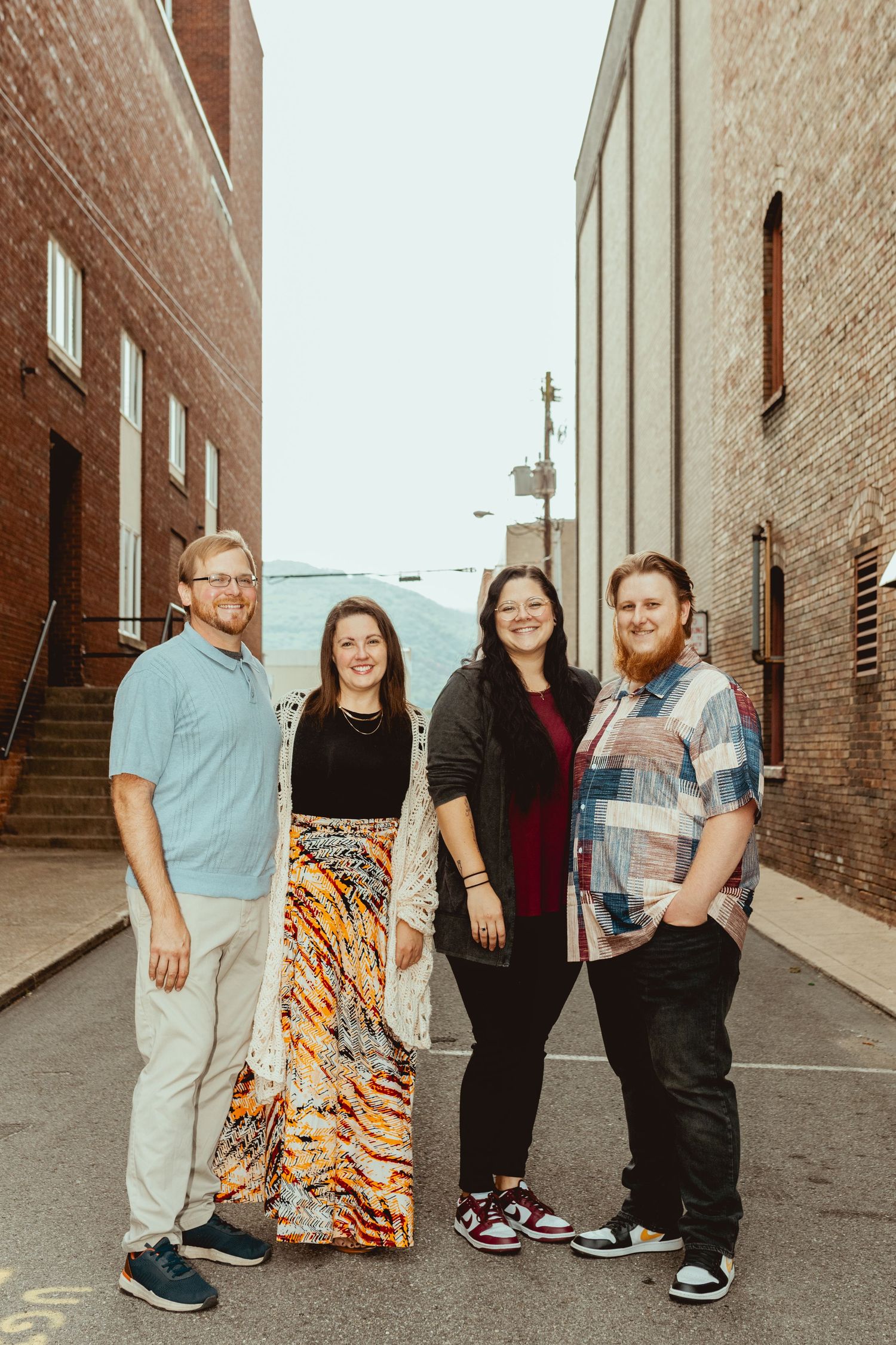 People stand together in a casual outdoor photoshoot against brick walls and an alley backdrop.