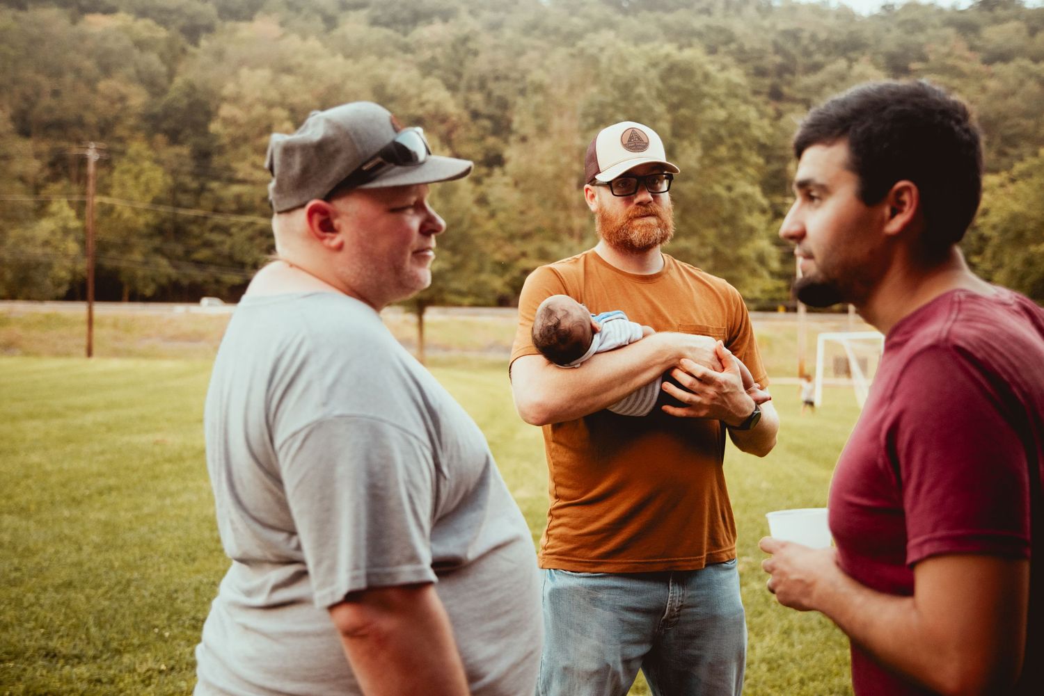 A group gathered outdoors in a grassy area having conversations and social interactions.
