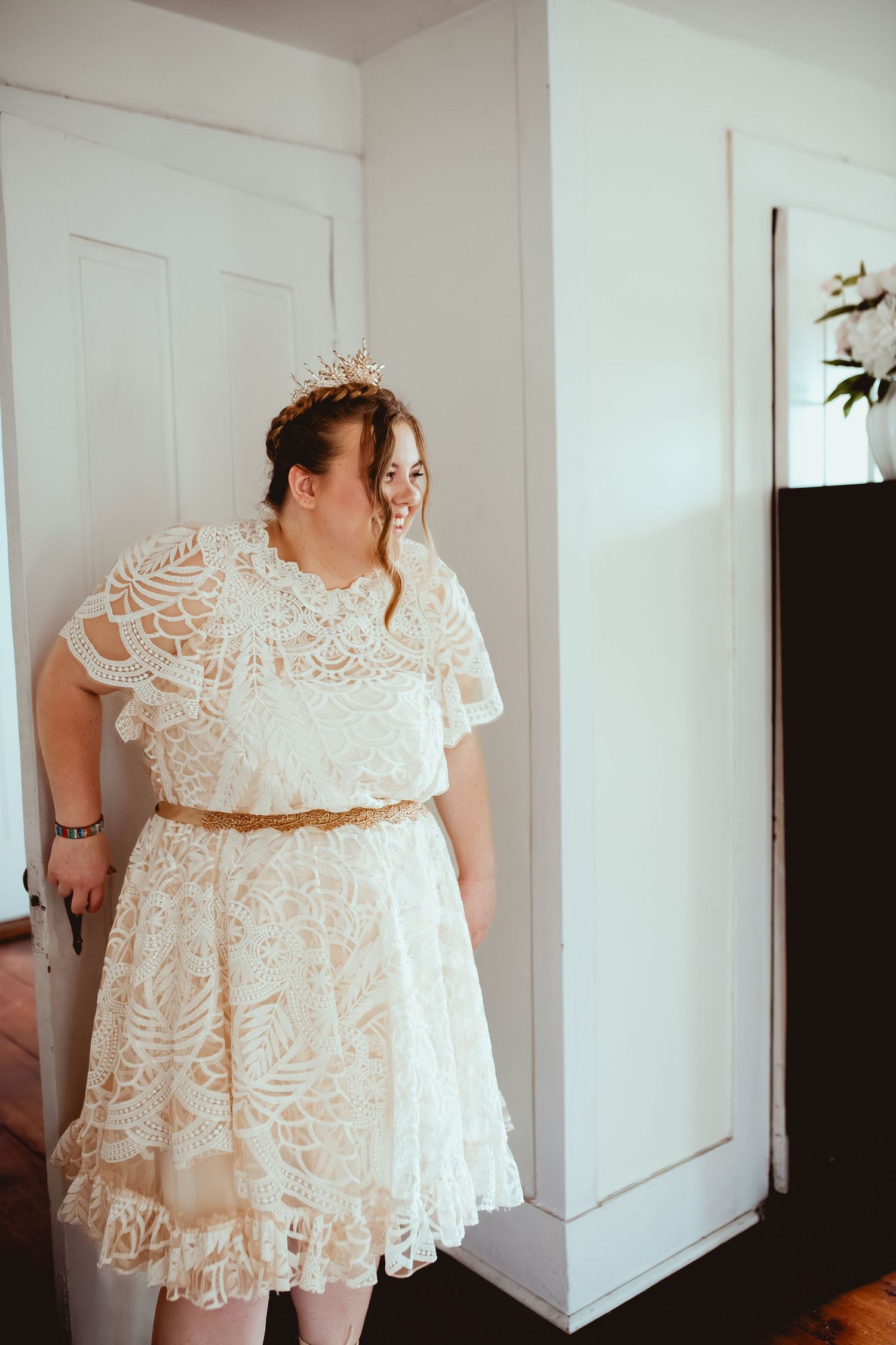 A delicate white lace wedding dress with short sleeves is displayed in a bright indoor setting.