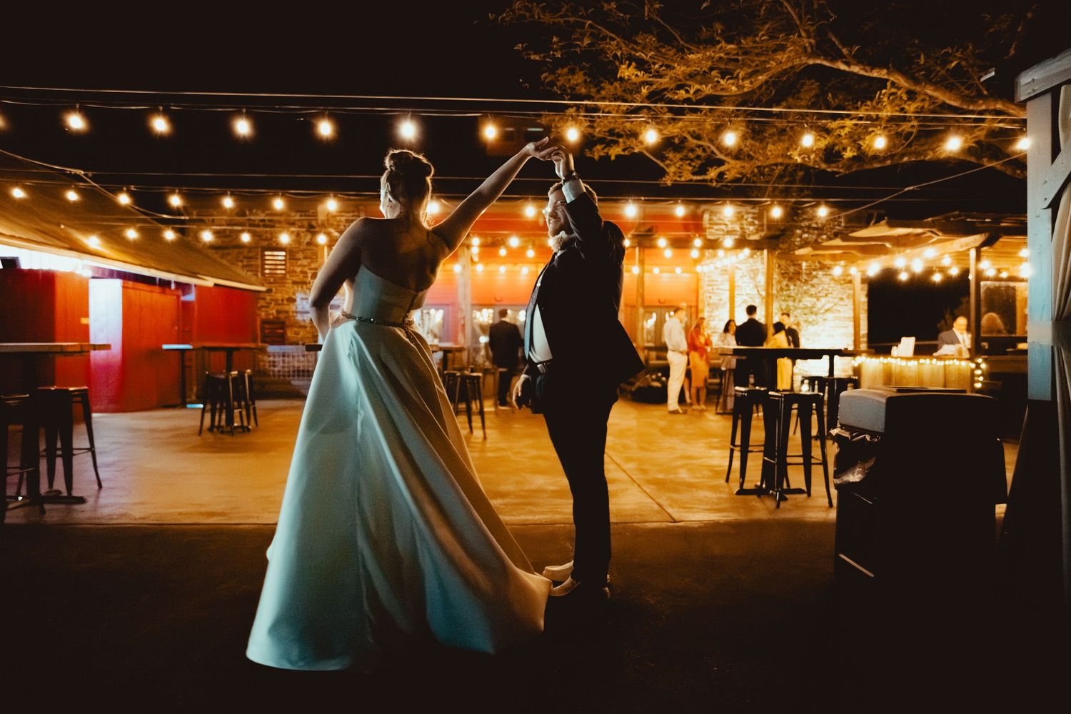 Bride and groom share first dance under string lights at romantic outdoor wedding venue at night.