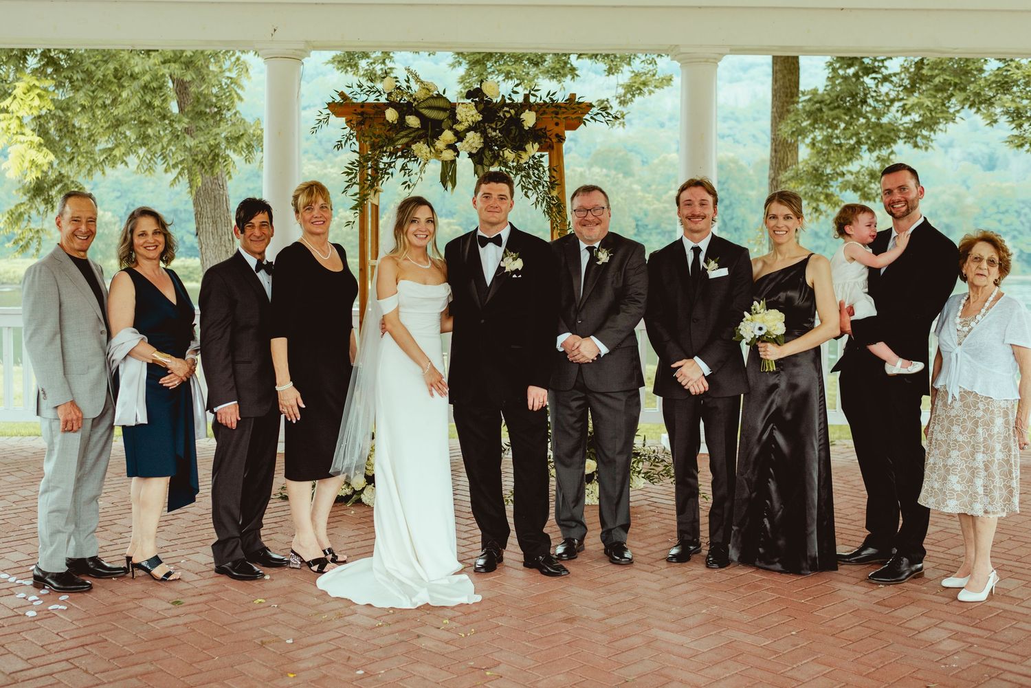 Wedding party poses under covered outdoor porch with greenery in background.
