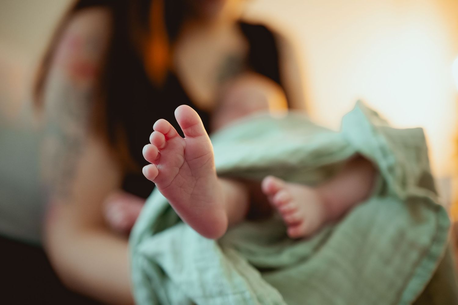 Close-up view of tiny baby feet wrapped in soft mint green blanket with blurred background.