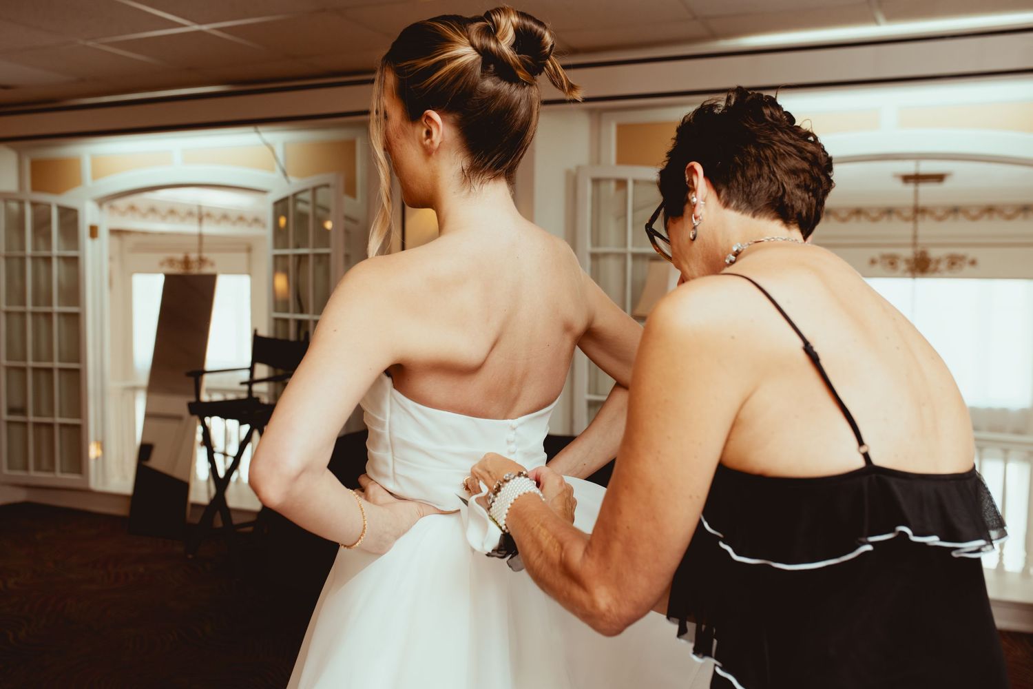 Two people adjusting a white wedding dress in an elegant room.